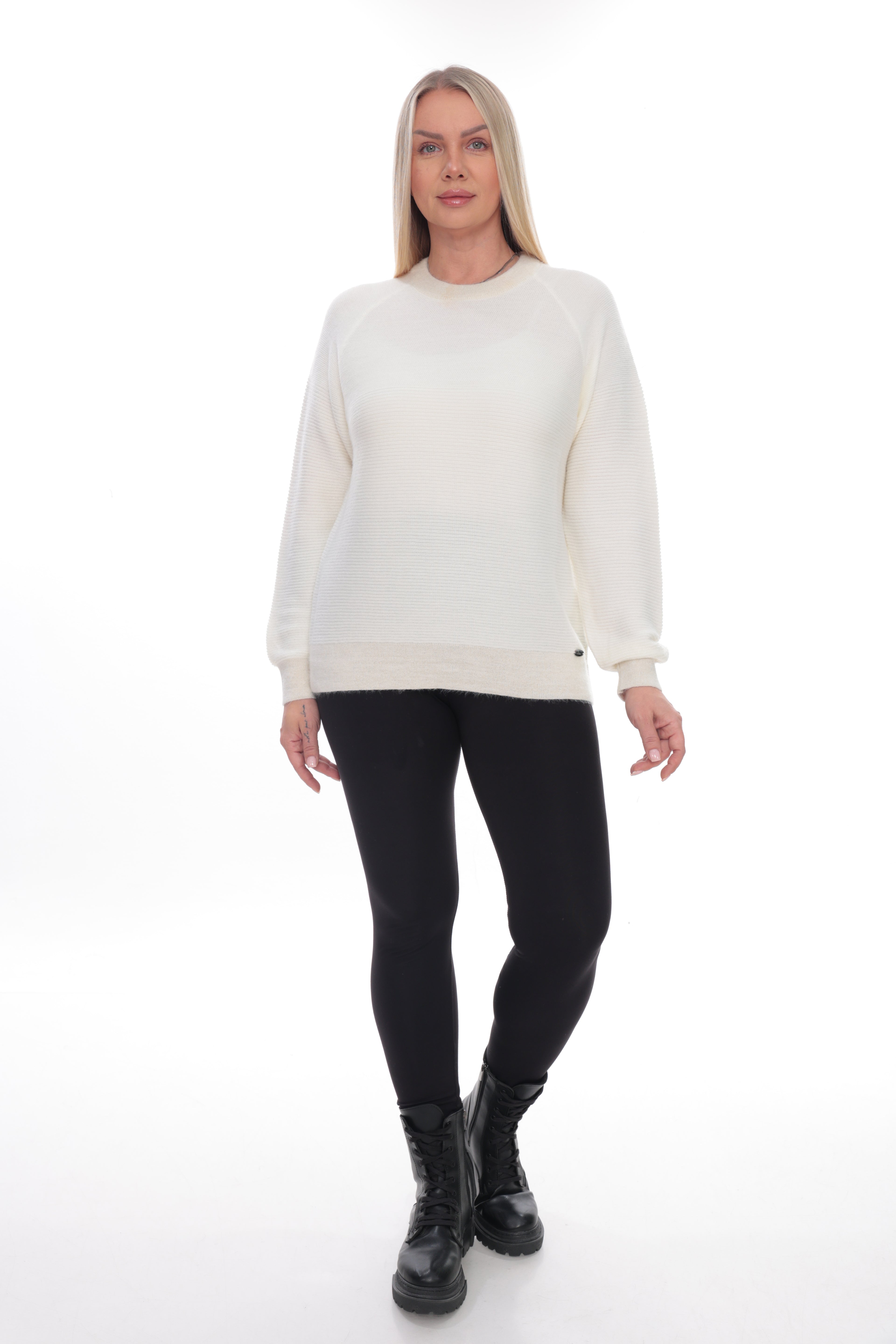 A woman modeling a cream-colored crewneck sweatshirt, paired with black leggings and black lace-up boots, against a solid white studio background.