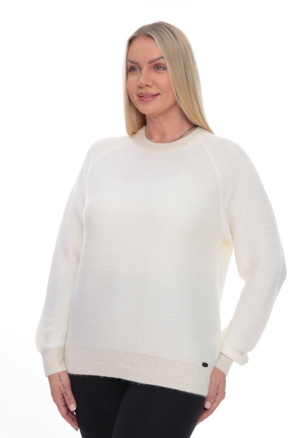 A blonde woman wearing a cream-colored ribbed knit crewneck sweater and black pants, standing against a plain white background.