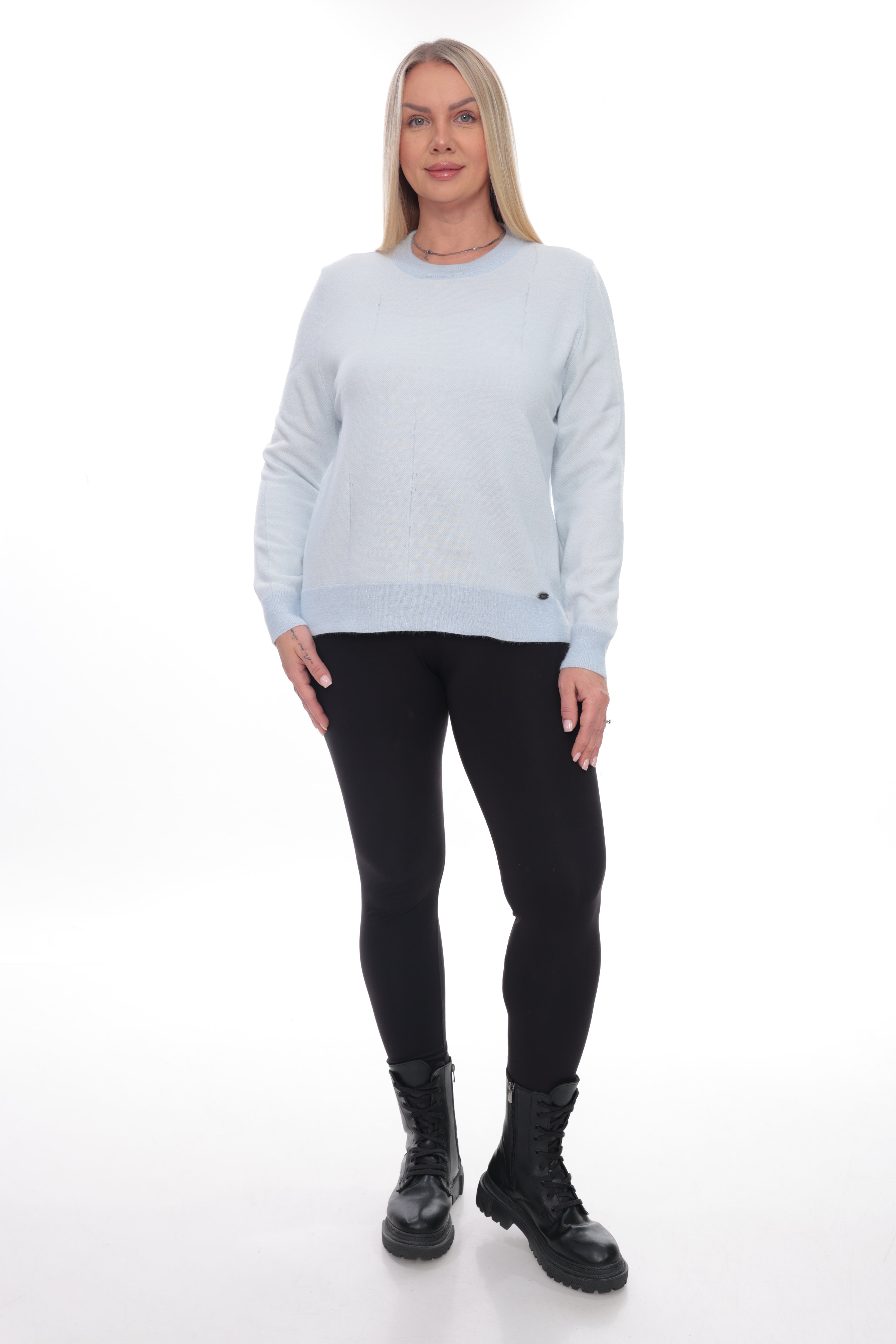 A woman modeling a light blue crewneck sweatshirt with black leggings and black combat boots, standing against a white studio background.