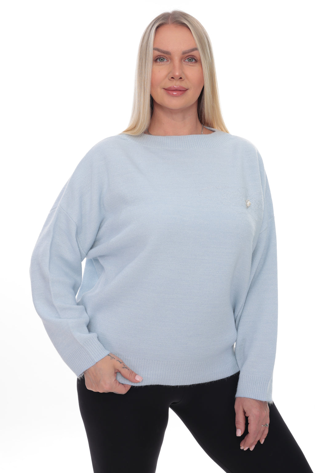A blonde woman modeling a light blue knit sweater with a small gold logo on the chest, paired with black pants, against a plain white background.