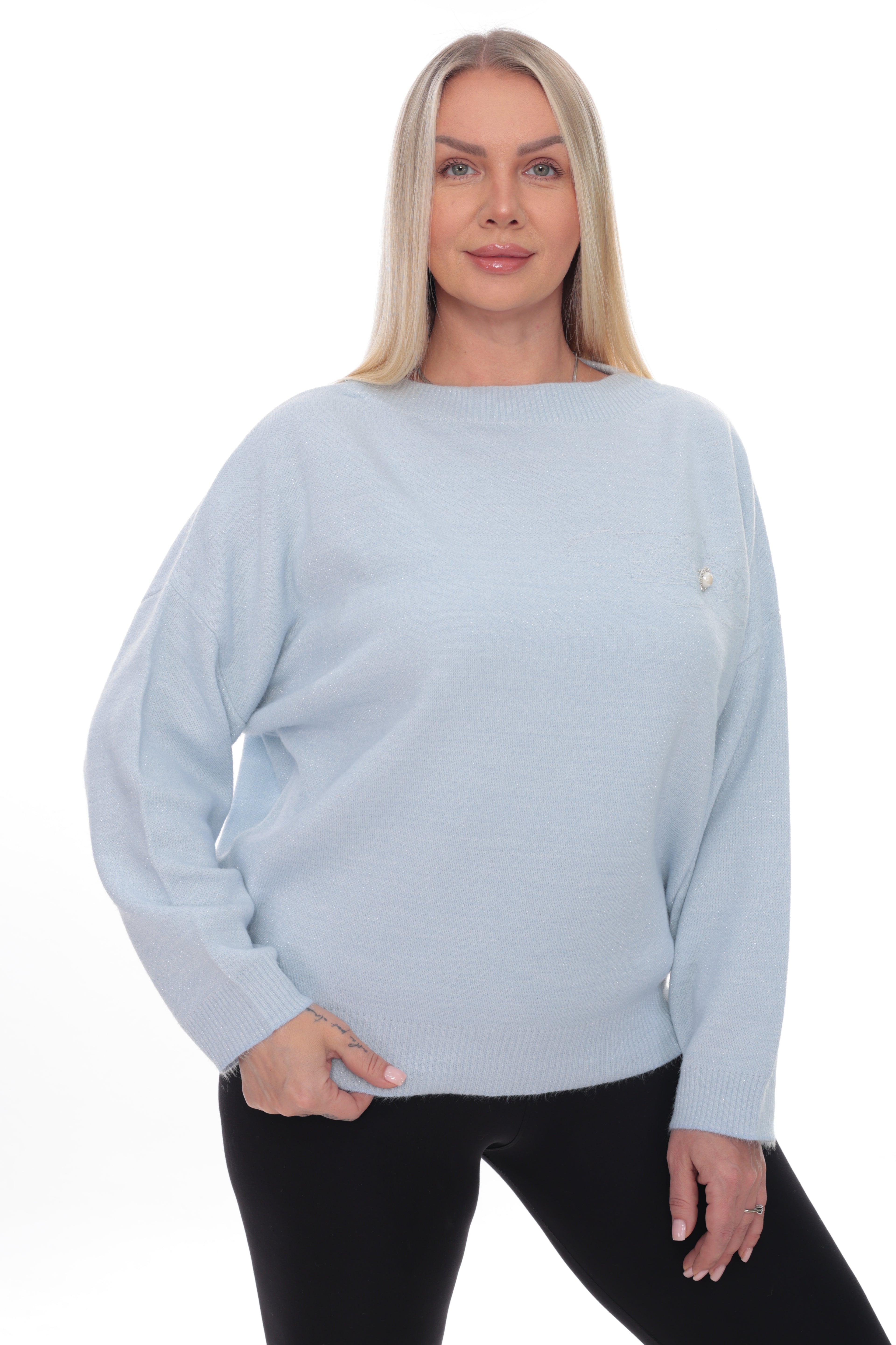 A blonde woman modeling a light blue knit sweater with a small gold logo on the chest, paired with black pants, against a plain white background.