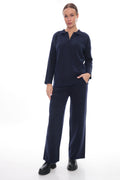 A woman modeling a matching navy blue knit lounge set consisting of a long-sleeve polo-neck top and wide-leg trousers, paired with black shoes, against a plain white studio background.