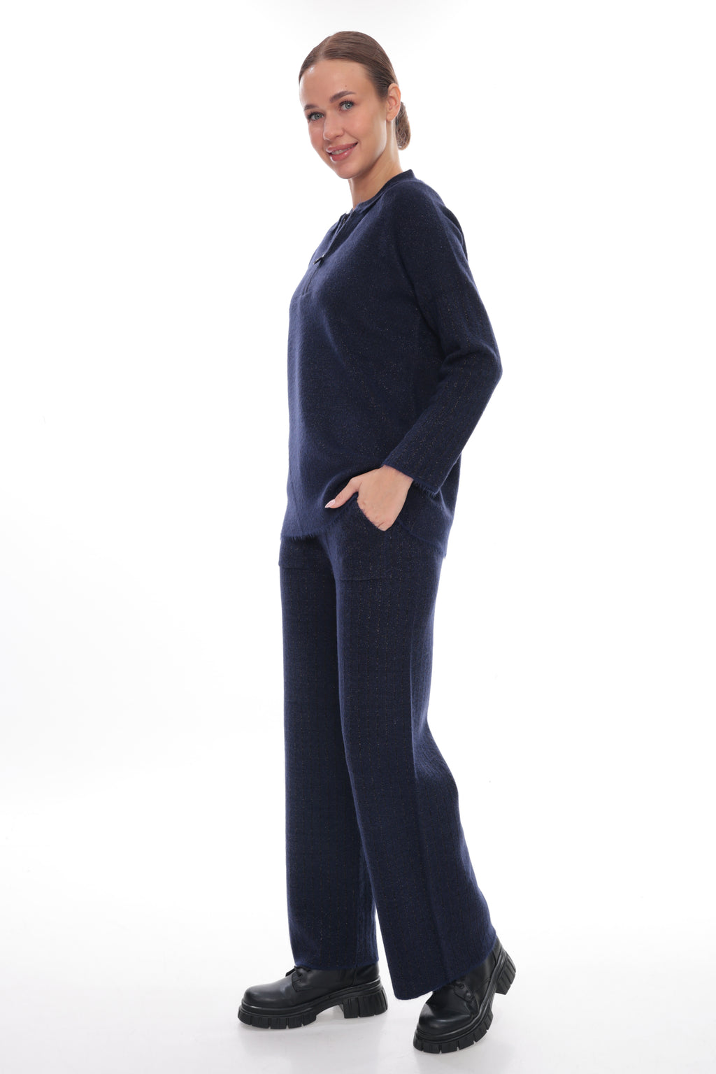 A woman modeling a matching navy blue knit lounge set consisting of a long-sleeve top and wide-leg trousers, paired with black platform shoes, against a solid white studio background.