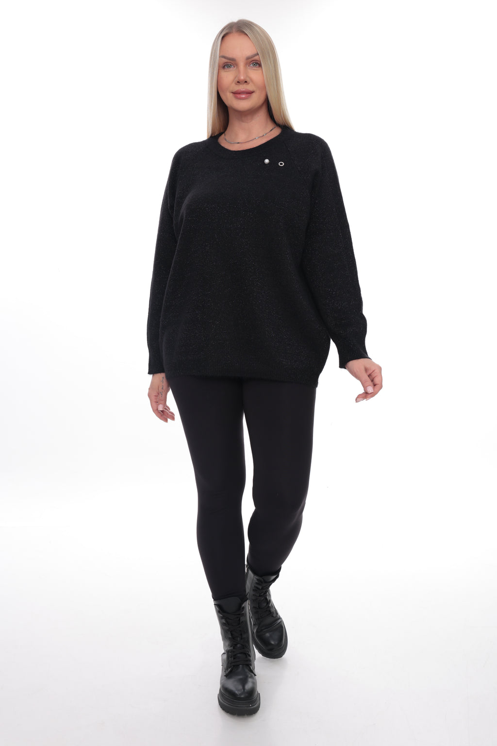 A woman modeling a black long-sleeve knit sweater with two small silver decorative studs on the chest, paired with black leggings and black boots, against a plain white studio background.
