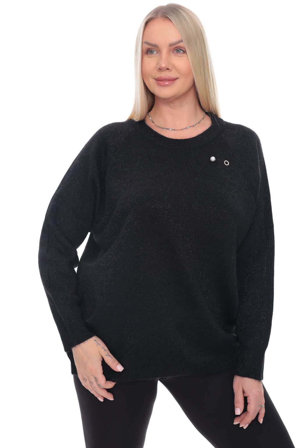 A blonde woman modeling a black knit crewneck sweater with a small silver button detail on the chest, paired with black leggings, against a plain white background.