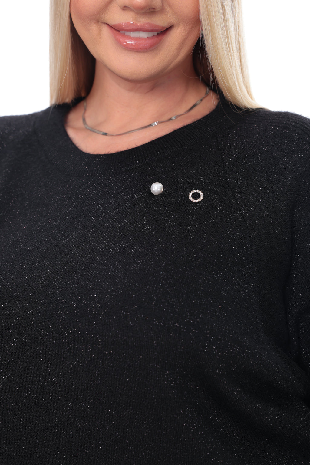 Close-up of a woman wearing a black knit sweater with two small silver chest pins, one oval and one ring-shaped, against a plain white background.