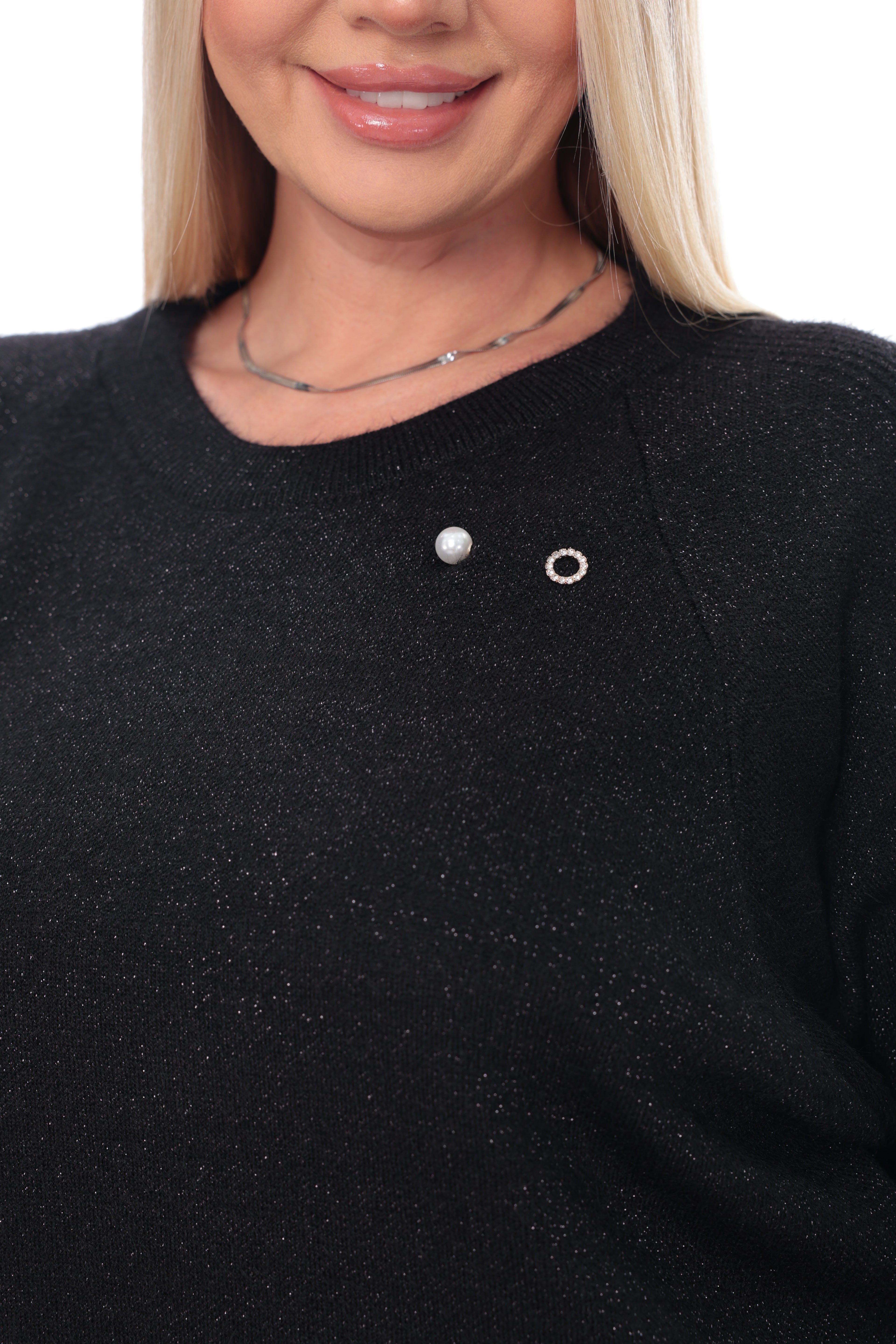 Close-up of a woman wearing a black knit sweater with two small silver chest pins, one oval and one ring-shaped, against a plain white background.
