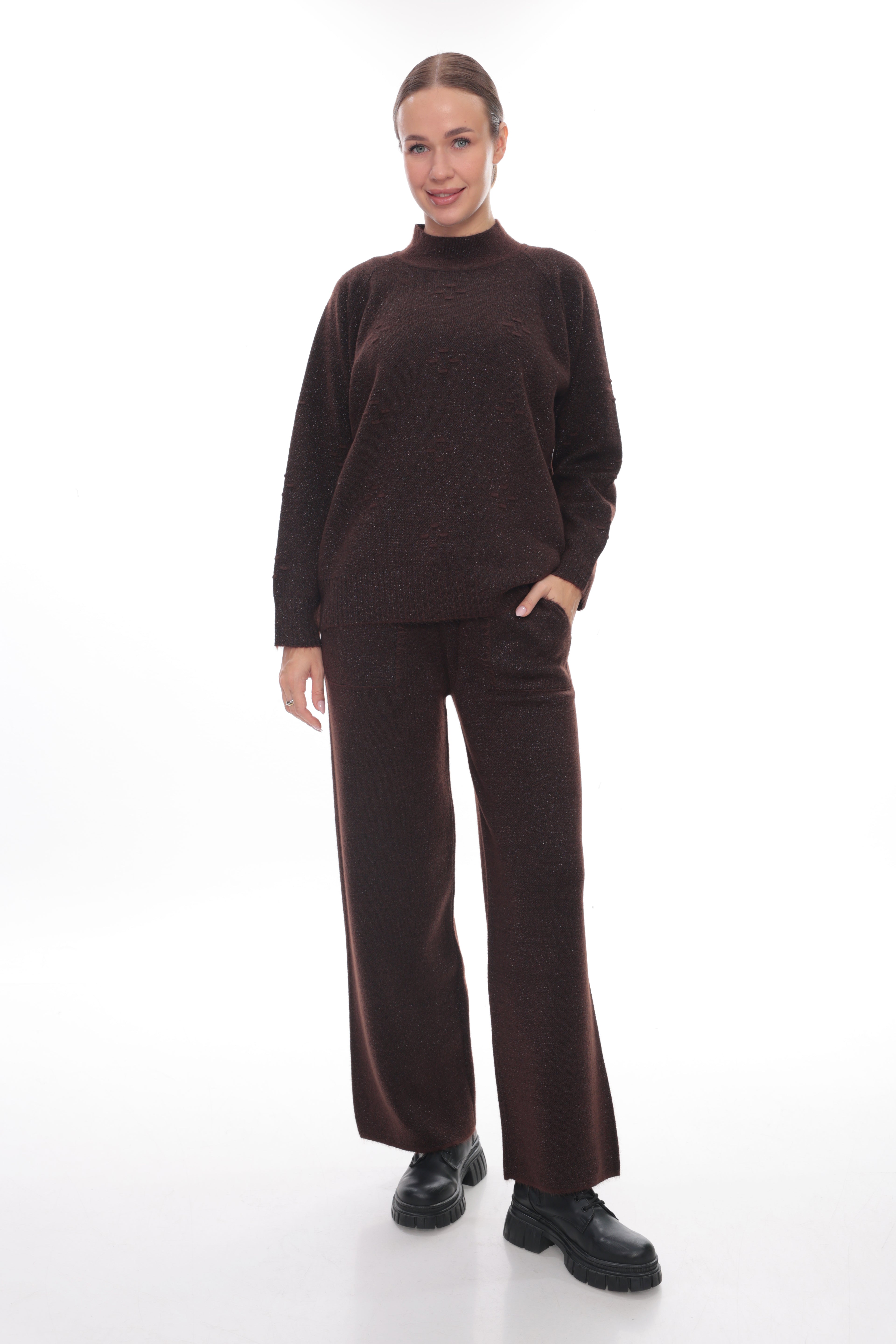 A woman modeling a dark brown knit two-piece set consisting of a mock neck long-sleeve sweater and matching wide-leg trousers, paired with black shoes, against a solid white studio background.