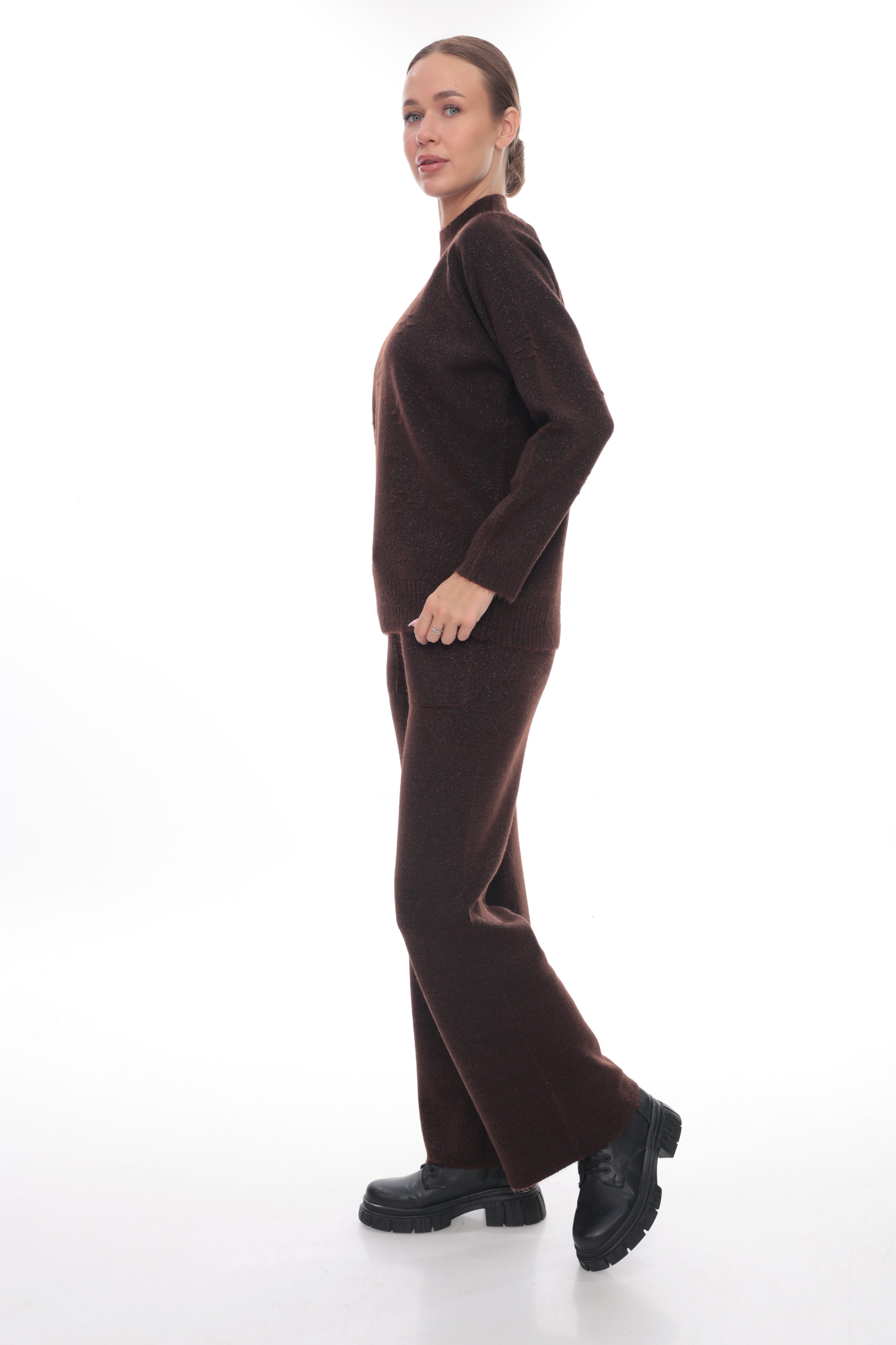 A woman modeling a dark brown knit matching set consisting of a mock-neck long-sleeve top and wide-leg trousers, paired with black platform shoes, against a solid white studio background.