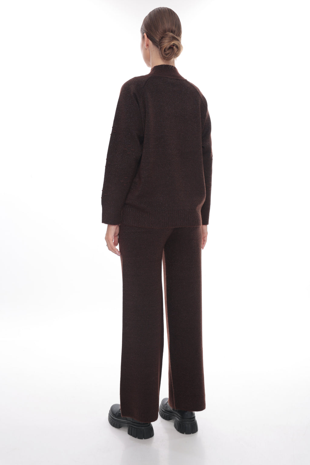 A model viewed from the back wearing a dark brown knit matching set consisting of a mock-neck long-sleeve top and wide-leg trousers, paired with black platform shoes on a white studio background.
