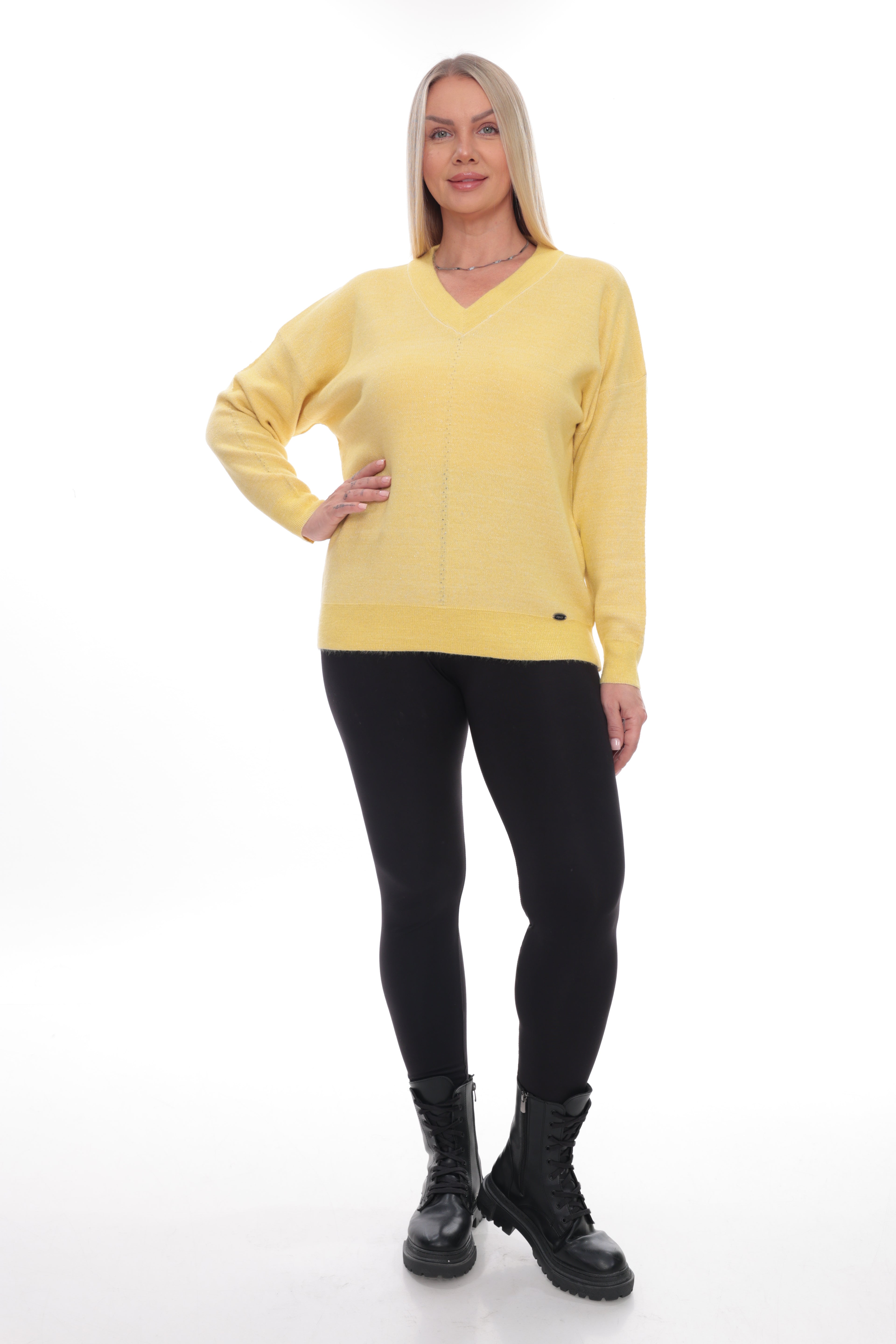 A blonde woman modeling a pale yellow V-neck knit sweater with long sleeves, paired with black leggings and black combat boots, against a plain white studio background.