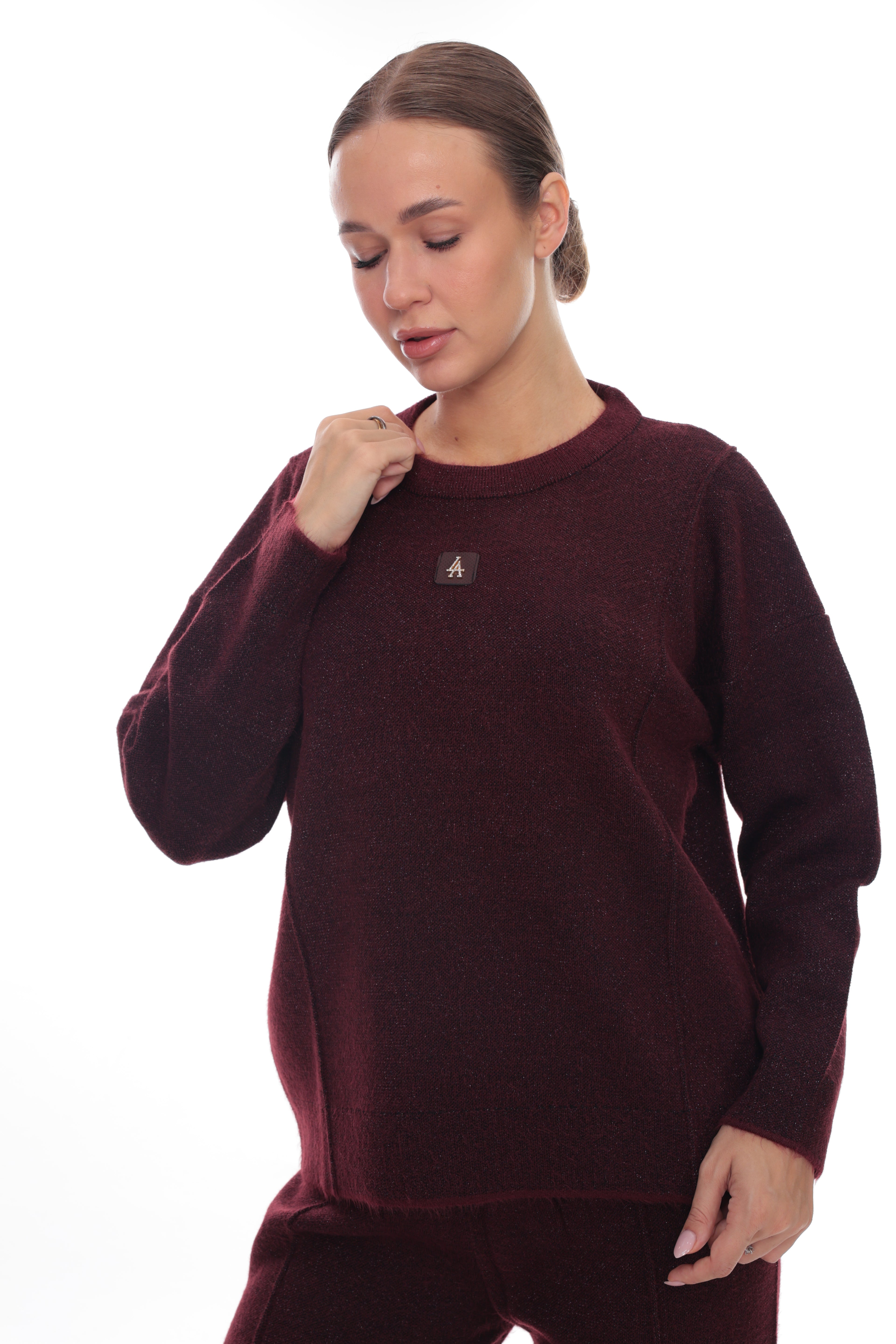 A woman wearing a dark burgundy knit crewneck sweater and matching pants, shown from the waist up against a plain white background.