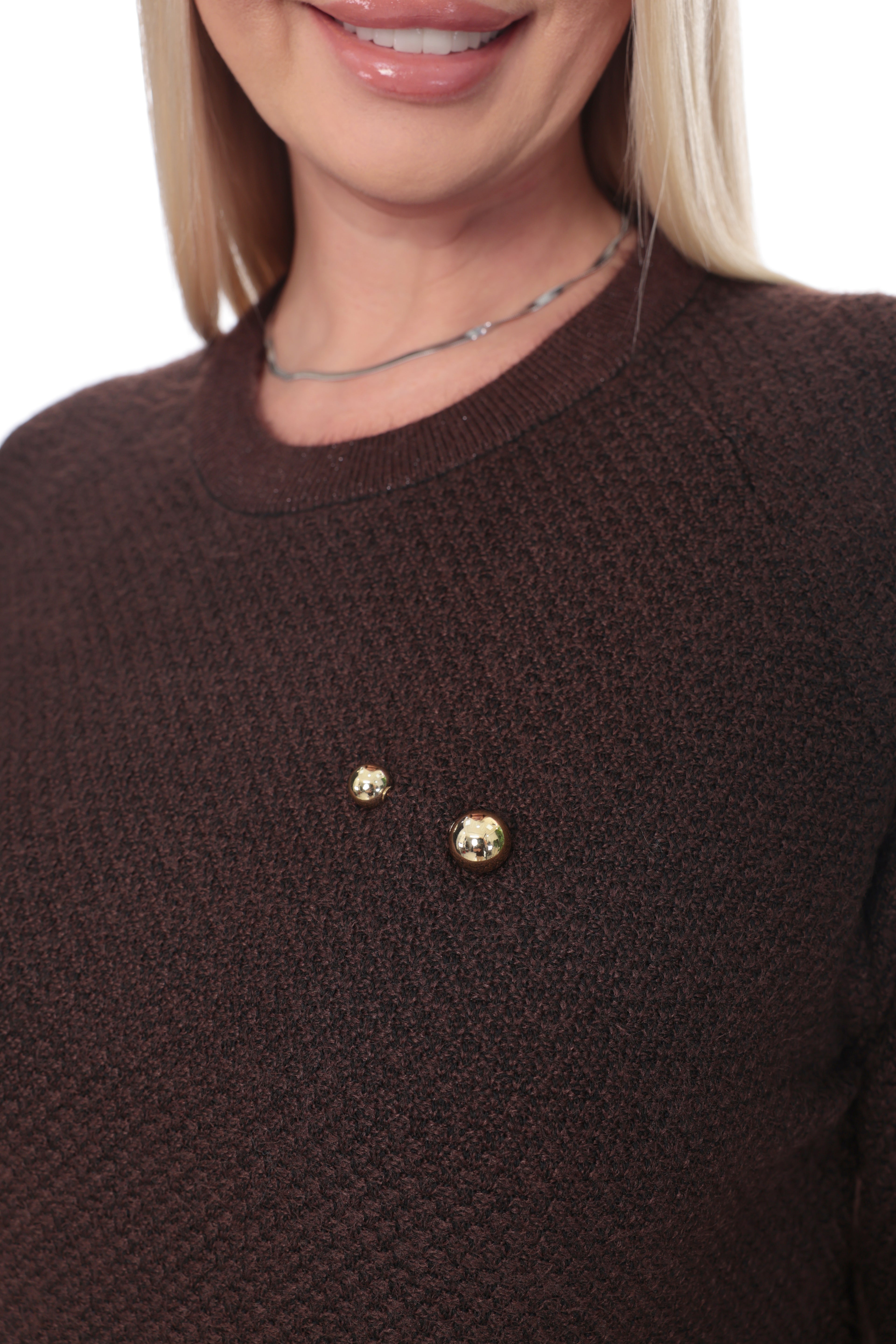 A close-up of a woman wearing a dark brown knit sweater and a delicate silver chain necklace with two small gold-tone stud earrings.