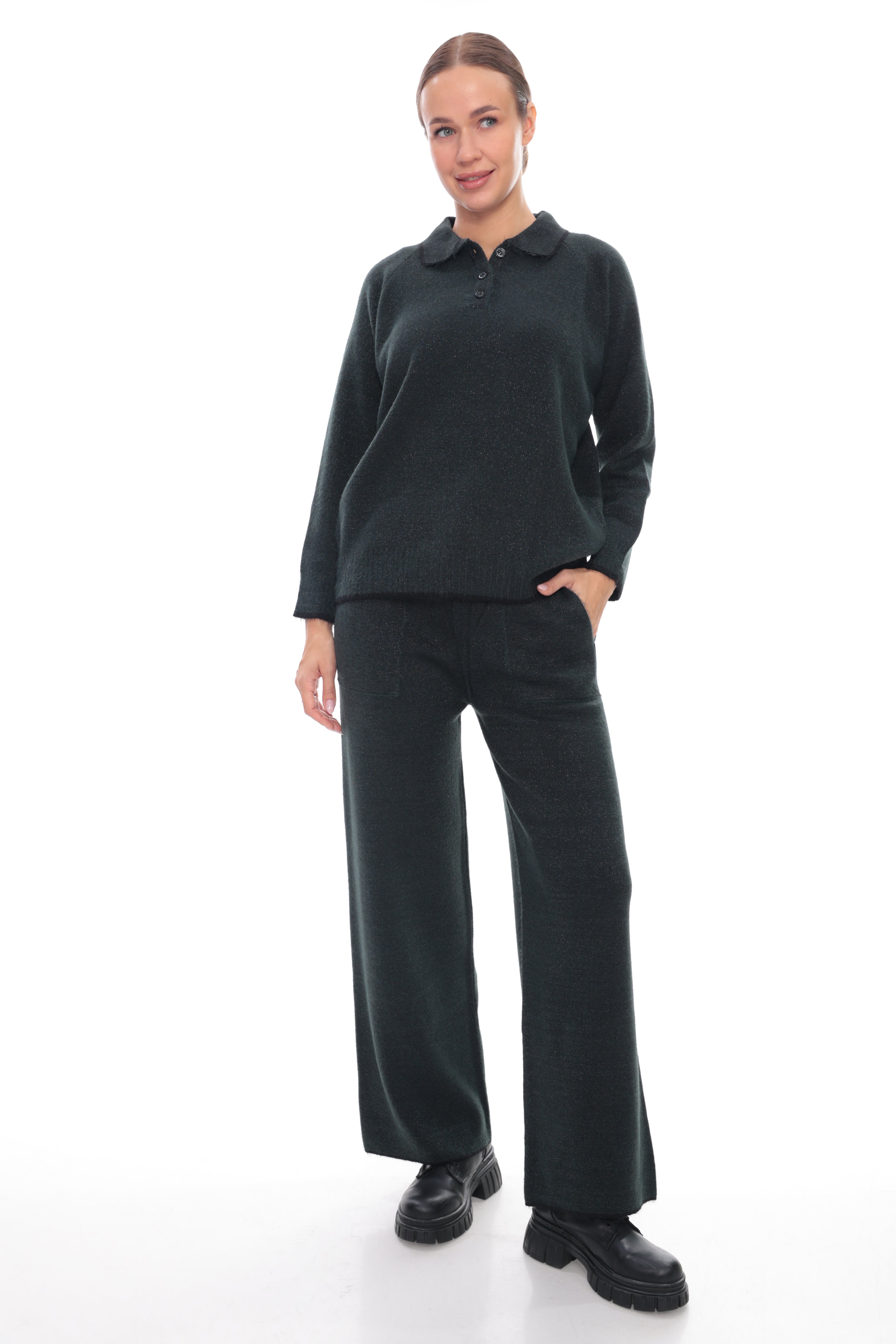 A woman modeling a dark charcoal green long-sleeve polo sweater and matching wide-leg trousers, paired with black shoes, against a plain white studio background.