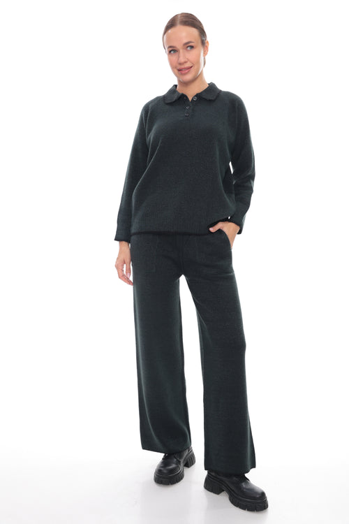 A woman modeling a dark charcoal green long-sleeve polo sweater and matching wide-leg trousers, paired with black shoes, against a plain white studio background.
