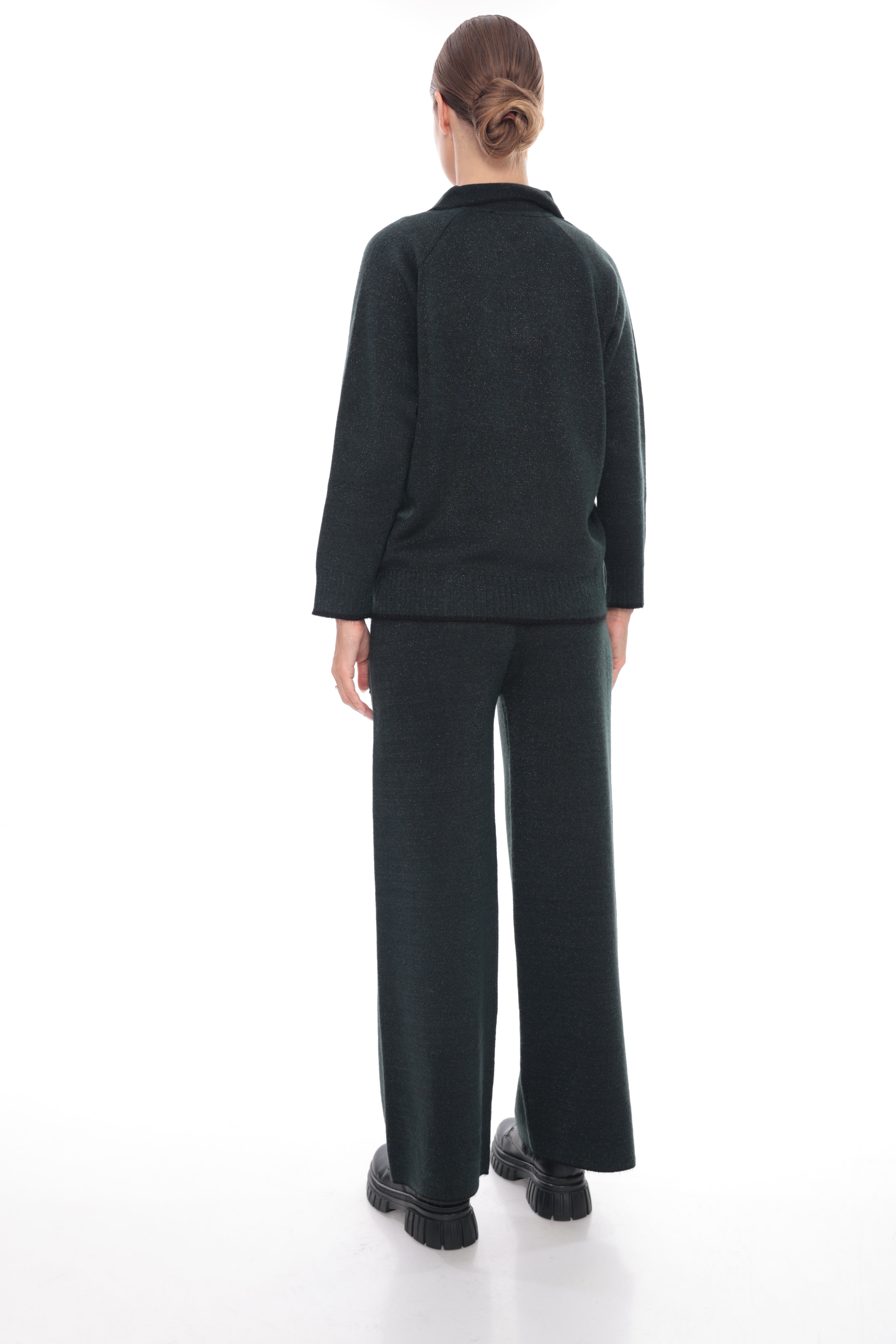 A model viewed from the back wearing a dark charcoal green knit top and matching wide-leg trousers, paired with black platform shoes, against a solid white studio background.