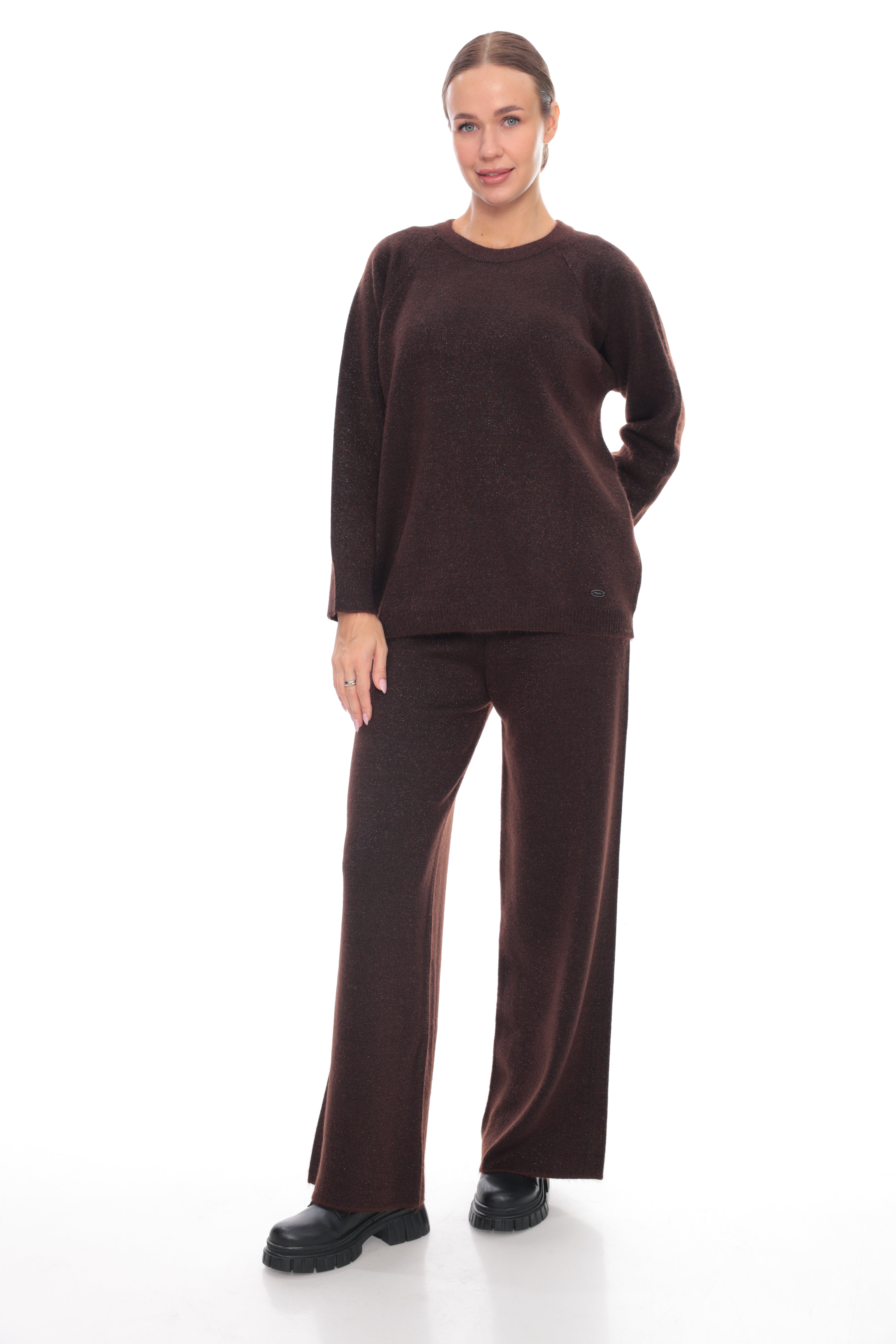 A woman modeling a matching dark brown knit loungewear set consisting of a long-sleeve crewneck sweater and wide-leg pants, paired with black platform shoes against a white studio background.