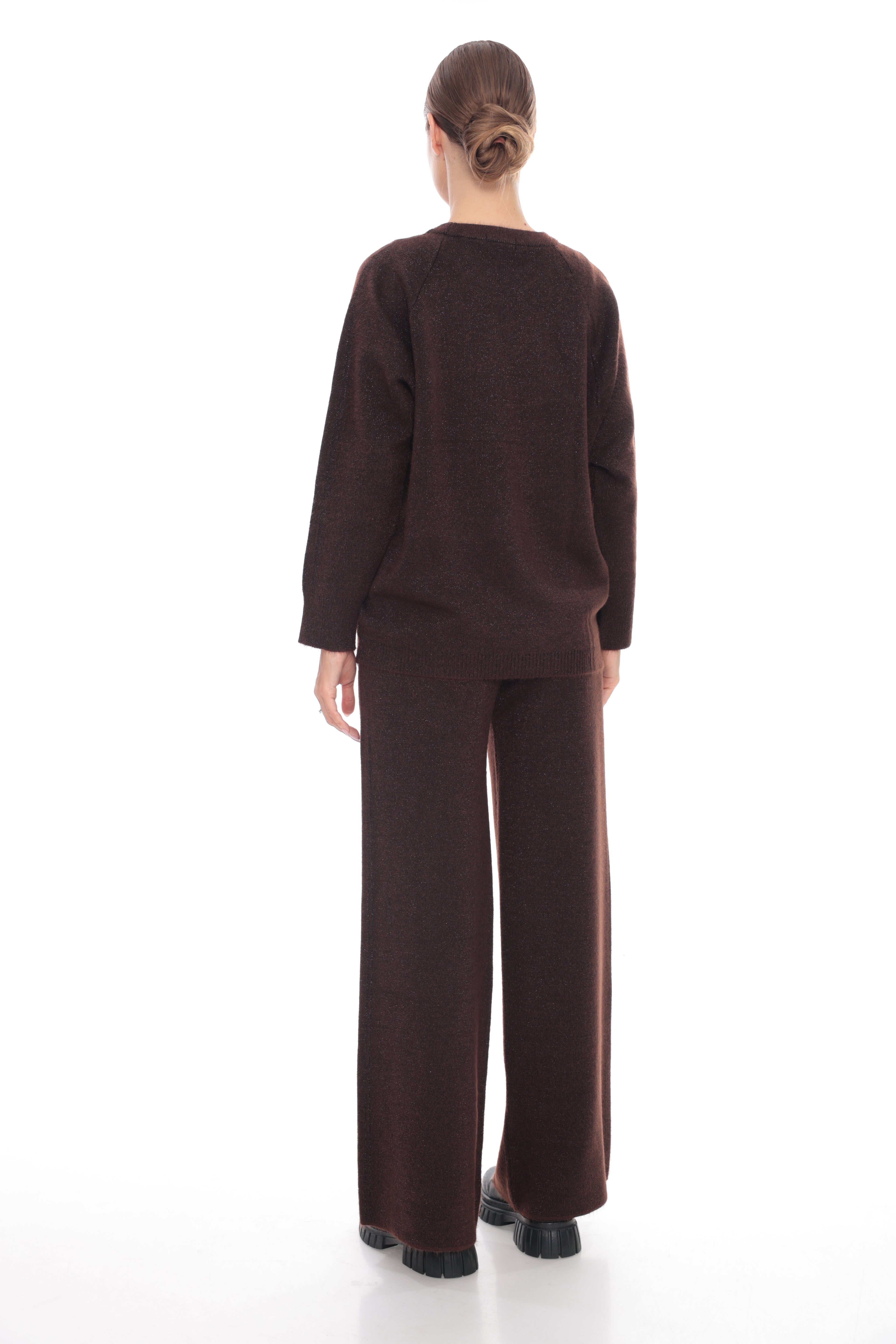 A model viewed from the back wearing a dark brown knit two-piece set consisting of a long-sleeve top and wide-leg trousers, set against a plain white studio background.