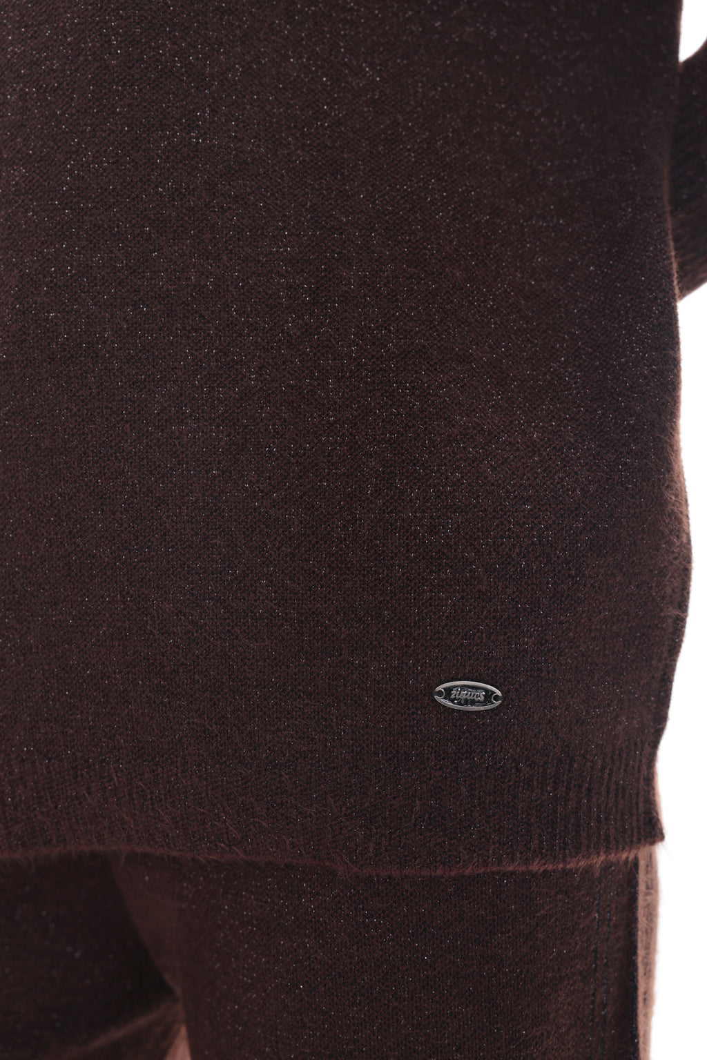Close-up of a dark brown knit sweater with a small oval logo patch near the hem, shown against a white background.