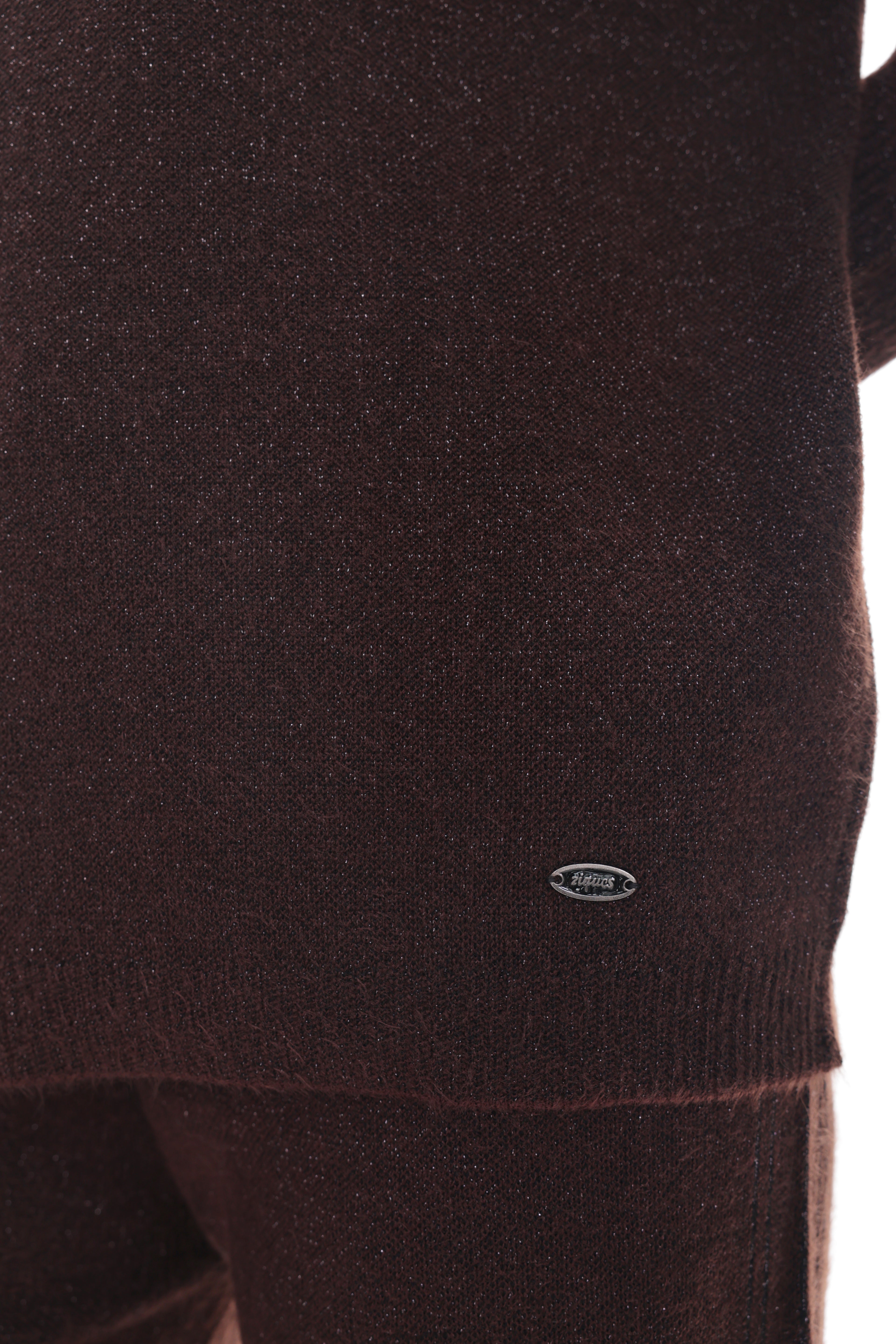 Close-up of a dark brown knit sweater with a small oval logo patch near the hem, shown against a white background.
