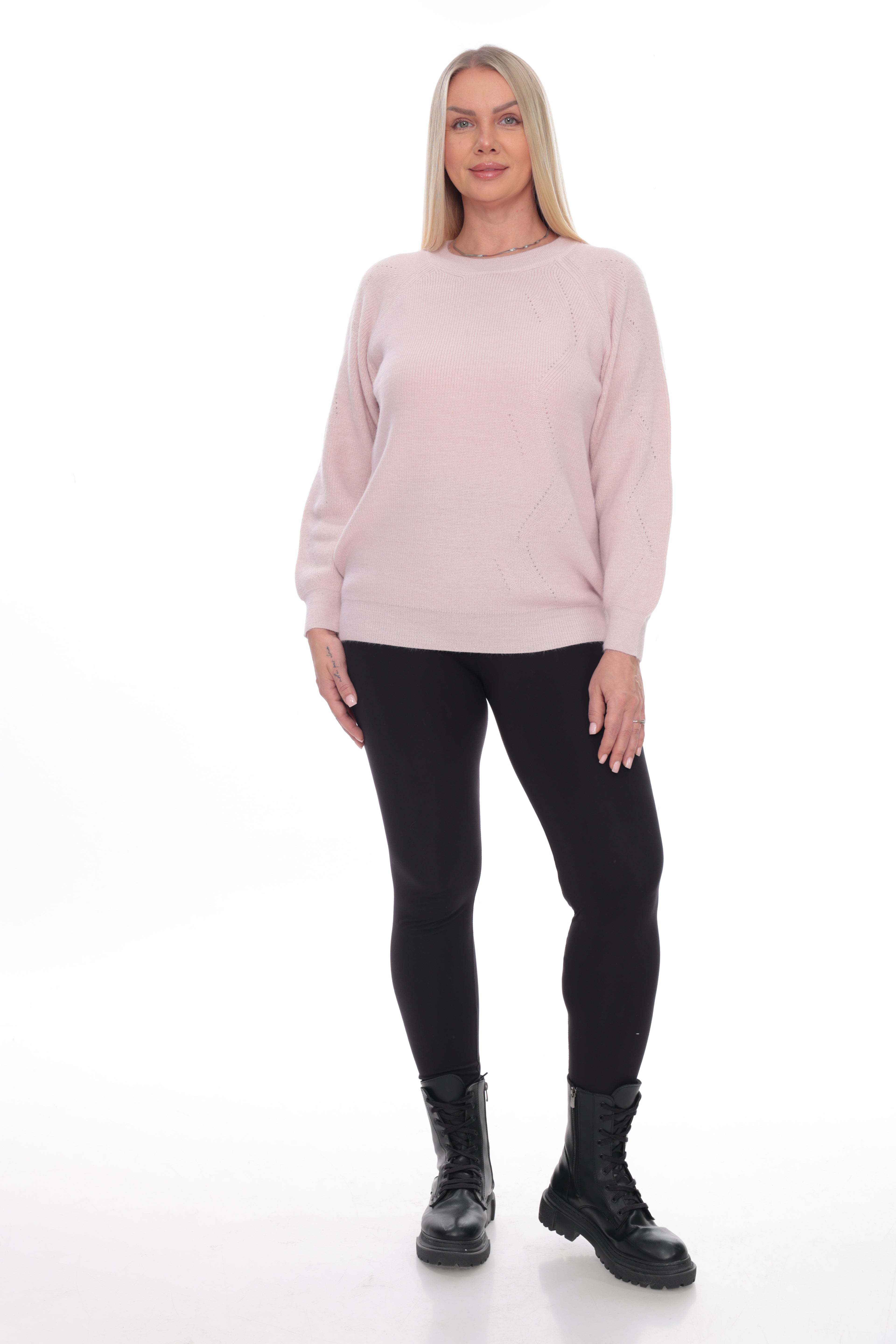 A woman modeling a light pink crewneck sweatshirt, paired with black leggings and black boots, against a plain white studio background.