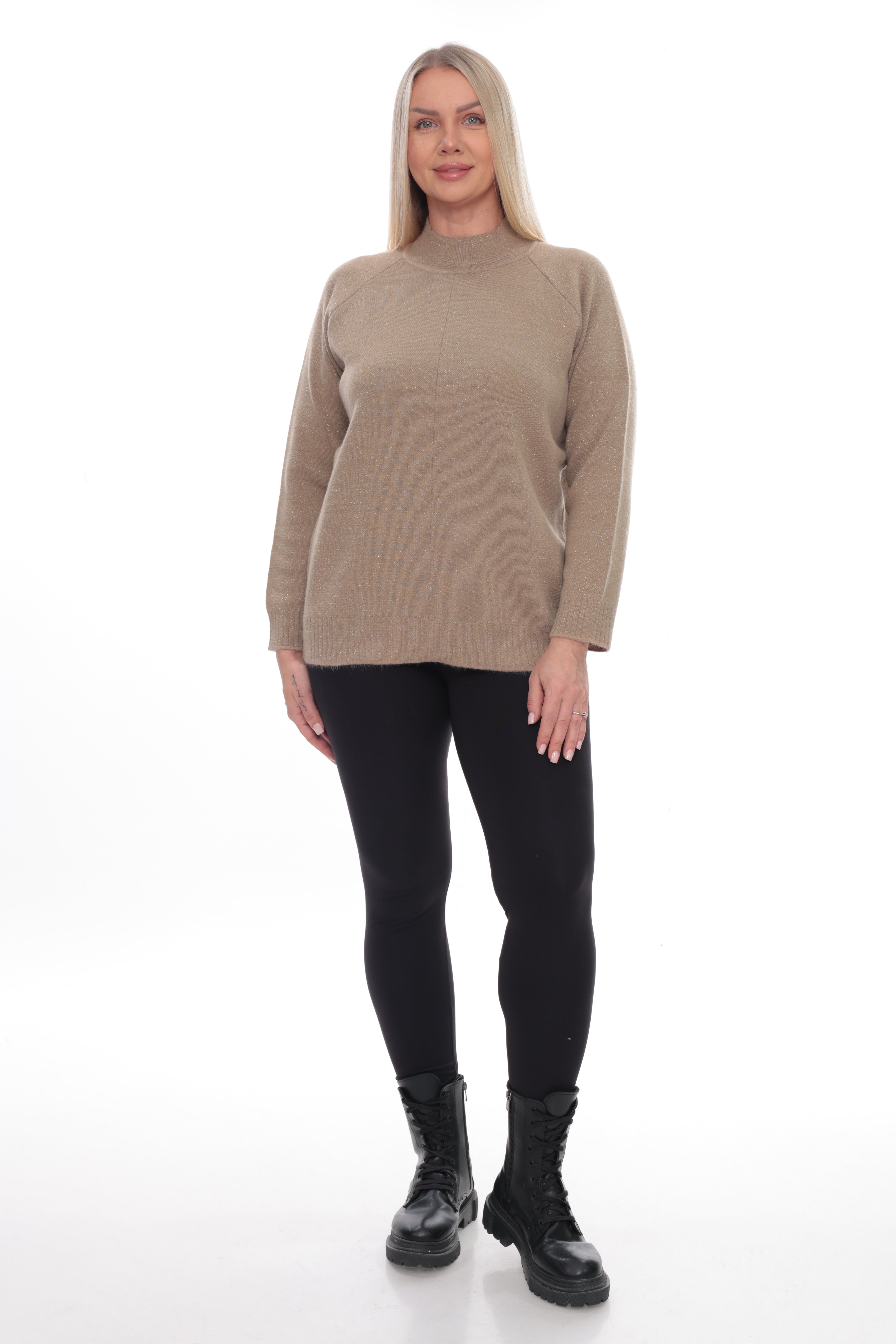 A woman modeling a beige mock-neck knit sweater with black leggings and black boots, standing against a plain white studio background.