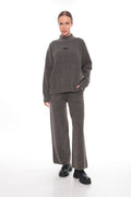 A woman modeling a matching dark brown knit two-piece set consisting of a mock-neck long-sleeve sweater and wide-leg trousers, paired with black shoes, against a plain white studio background.