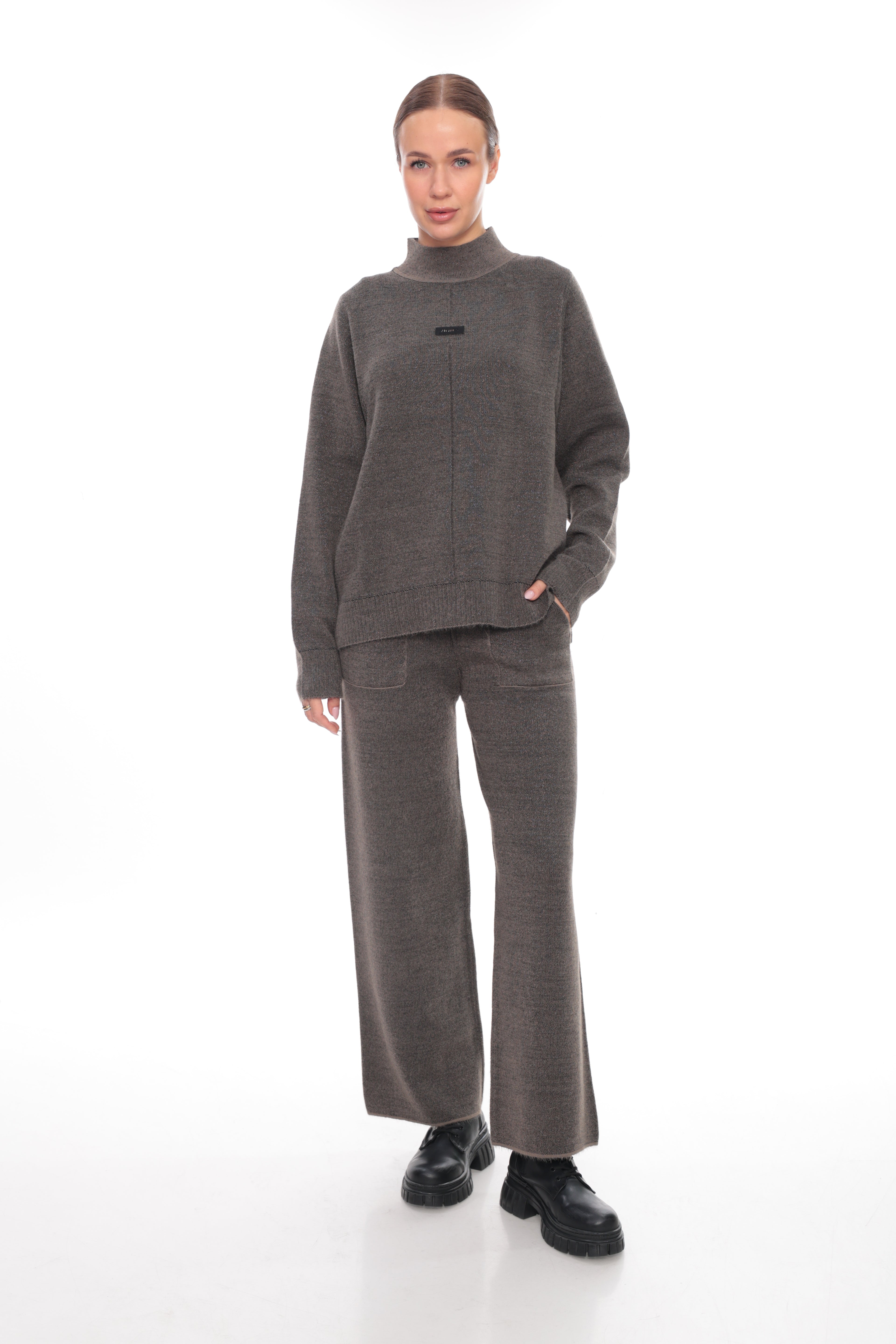 A woman modeling a matching dark brown knit two-piece set consisting of a mock-neck long-sleeve sweater and wide-leg trousers, paired with black shoes, against a plain white studio background.