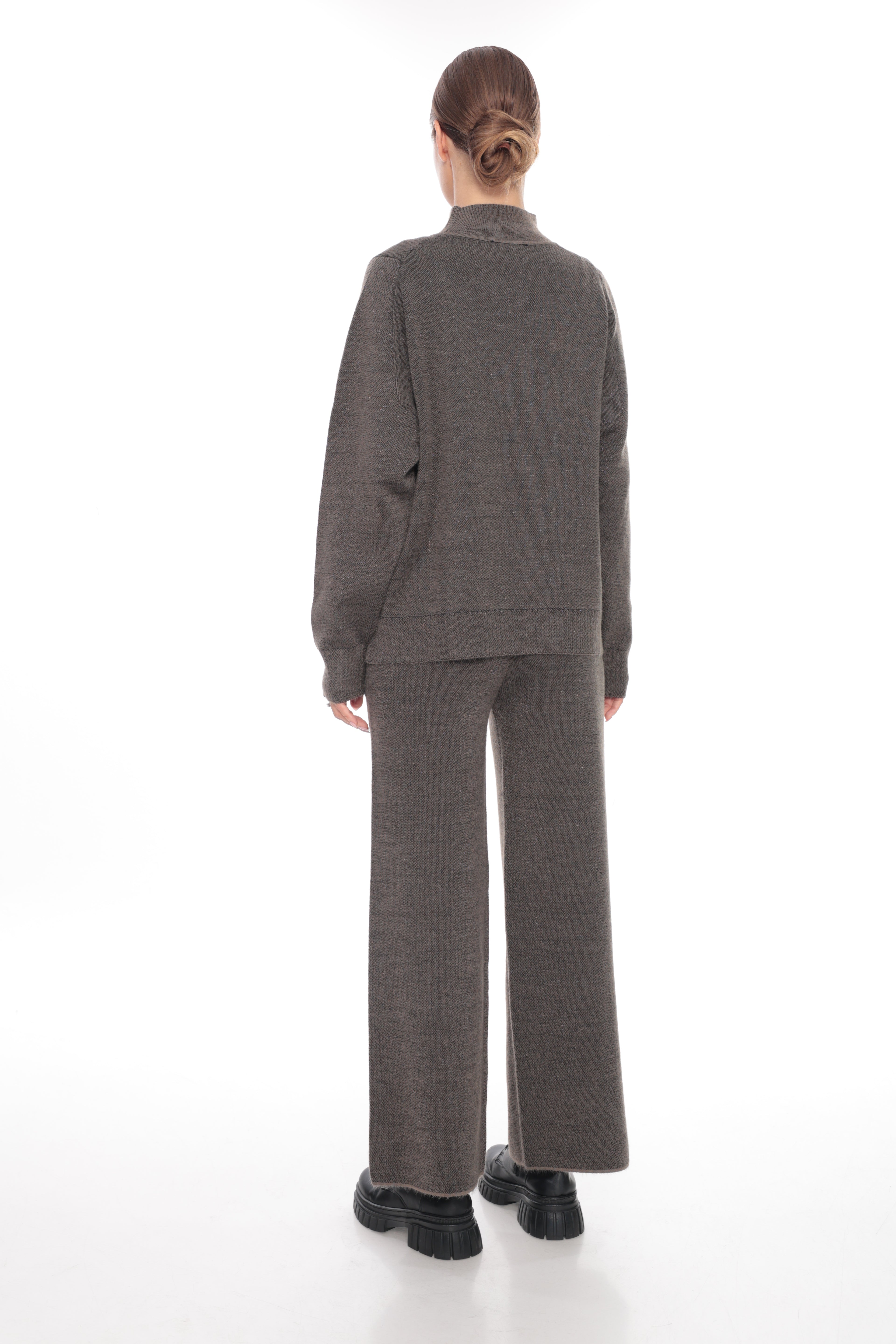 A model viewed from the back wearing a matching dark brown textured knit two-piece set consisting of a long-sleeve top and wide-leg trousers, paired with black platform shoes on a white studio background.