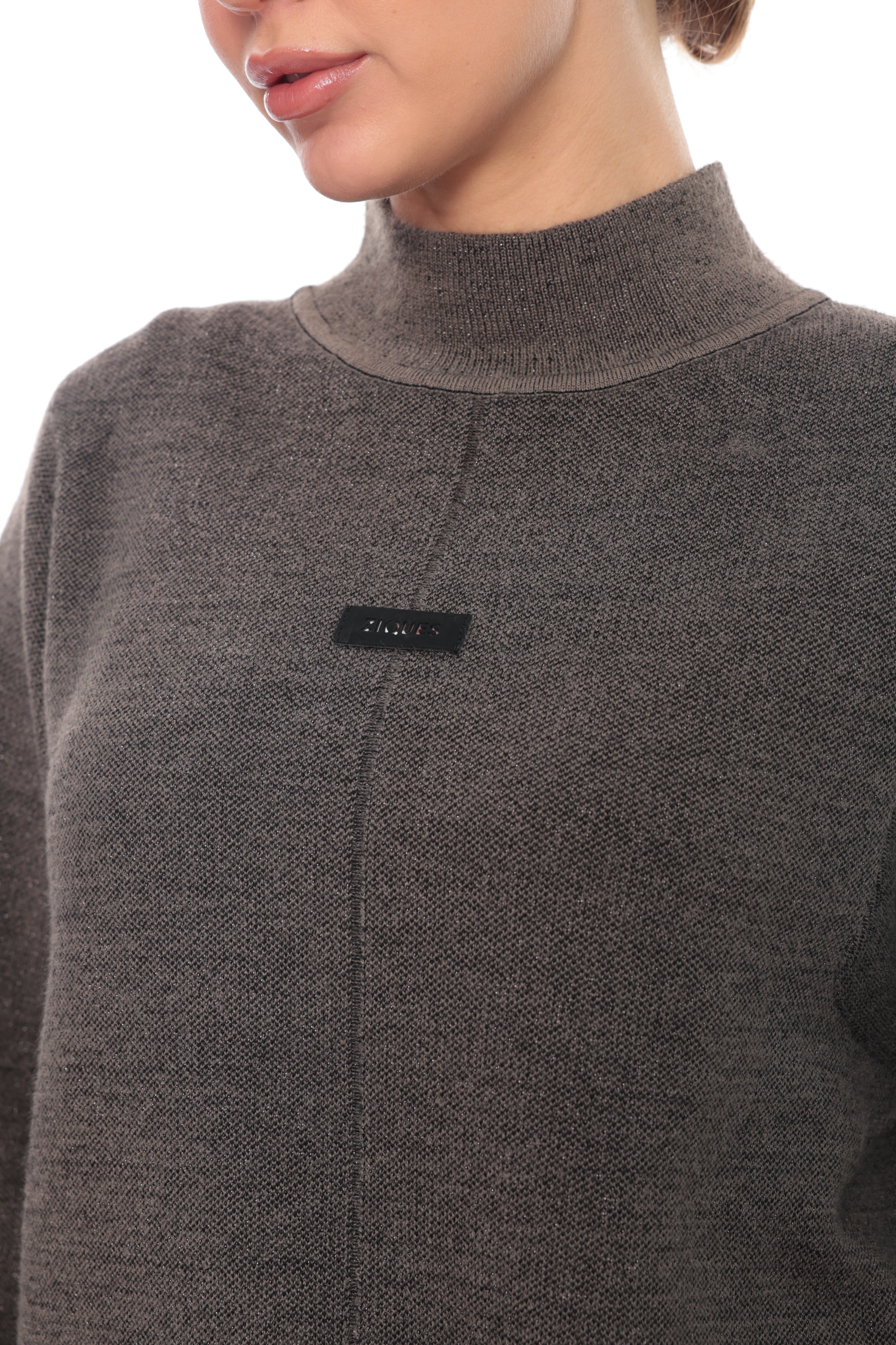 Close-up of a person wearing a dark gray ribbed knit mock neck sweater with a small black rectangular chest label.
