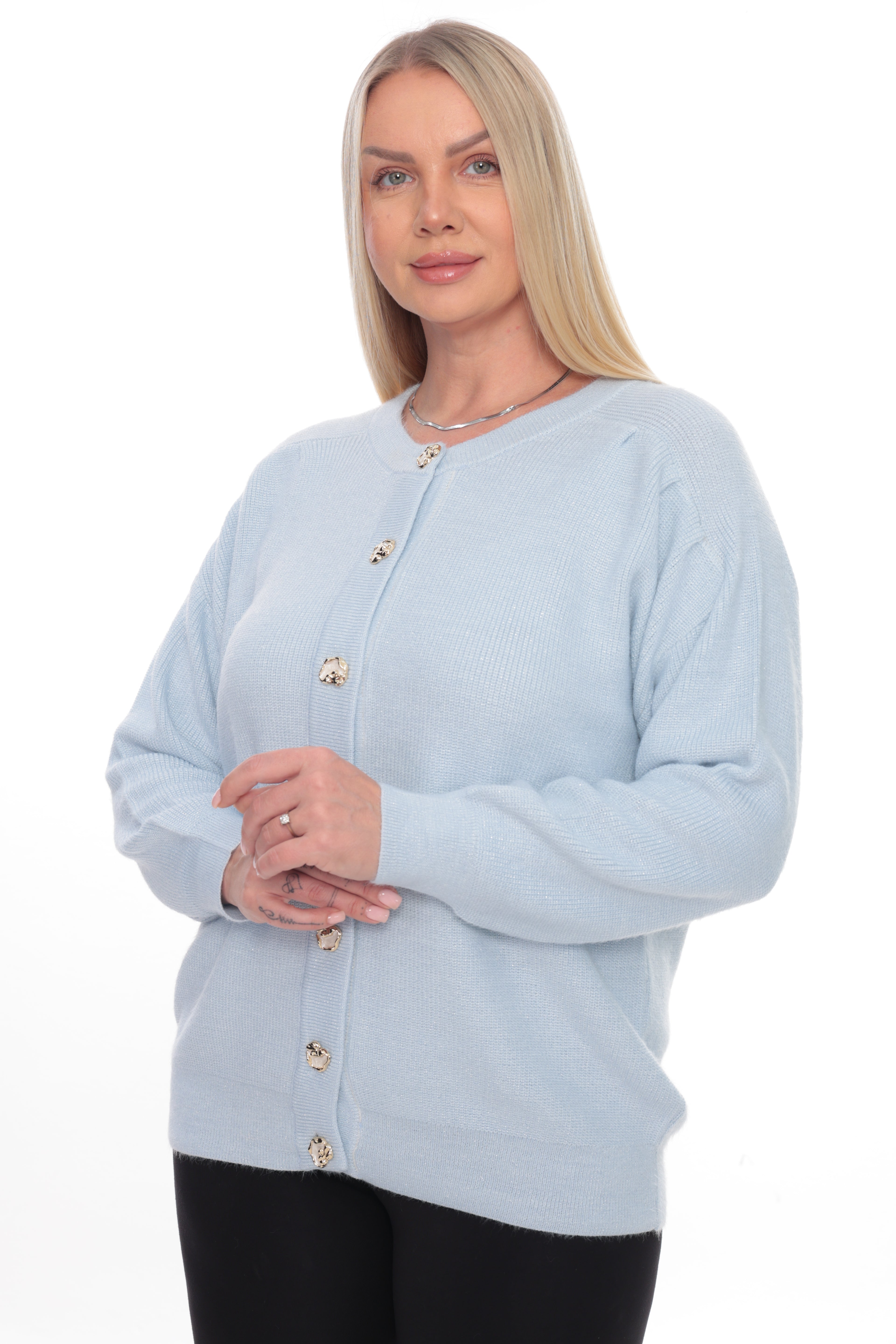 A blonde woman wearing a light blue ribbed knit cardigan sweater with decorative gold buttons, paired with black pants, against a plain white background.