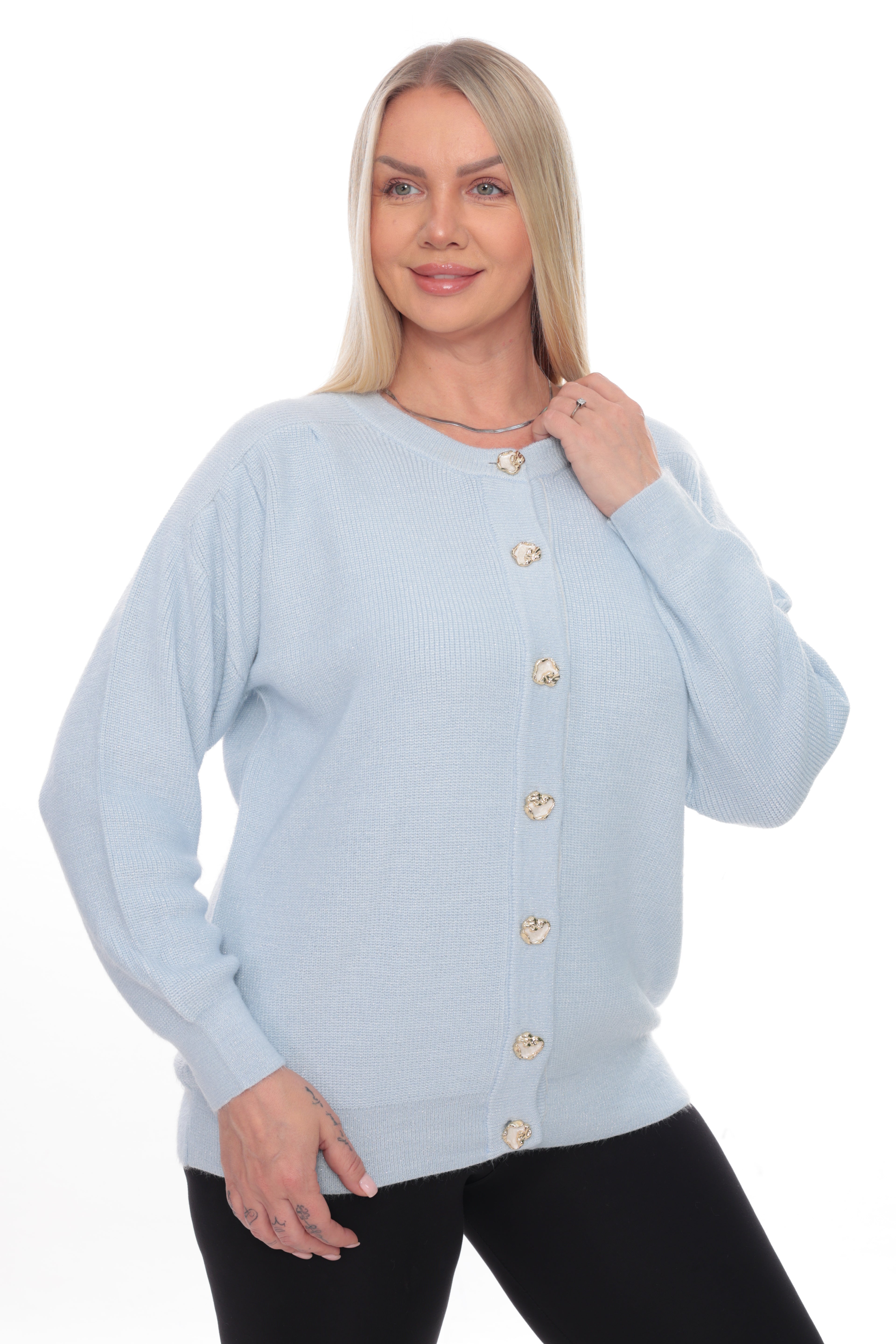 A blonde woman wearing a light blue long-sleeve knit cardigan with gold buttons, paired with black pants, against a plain white background.