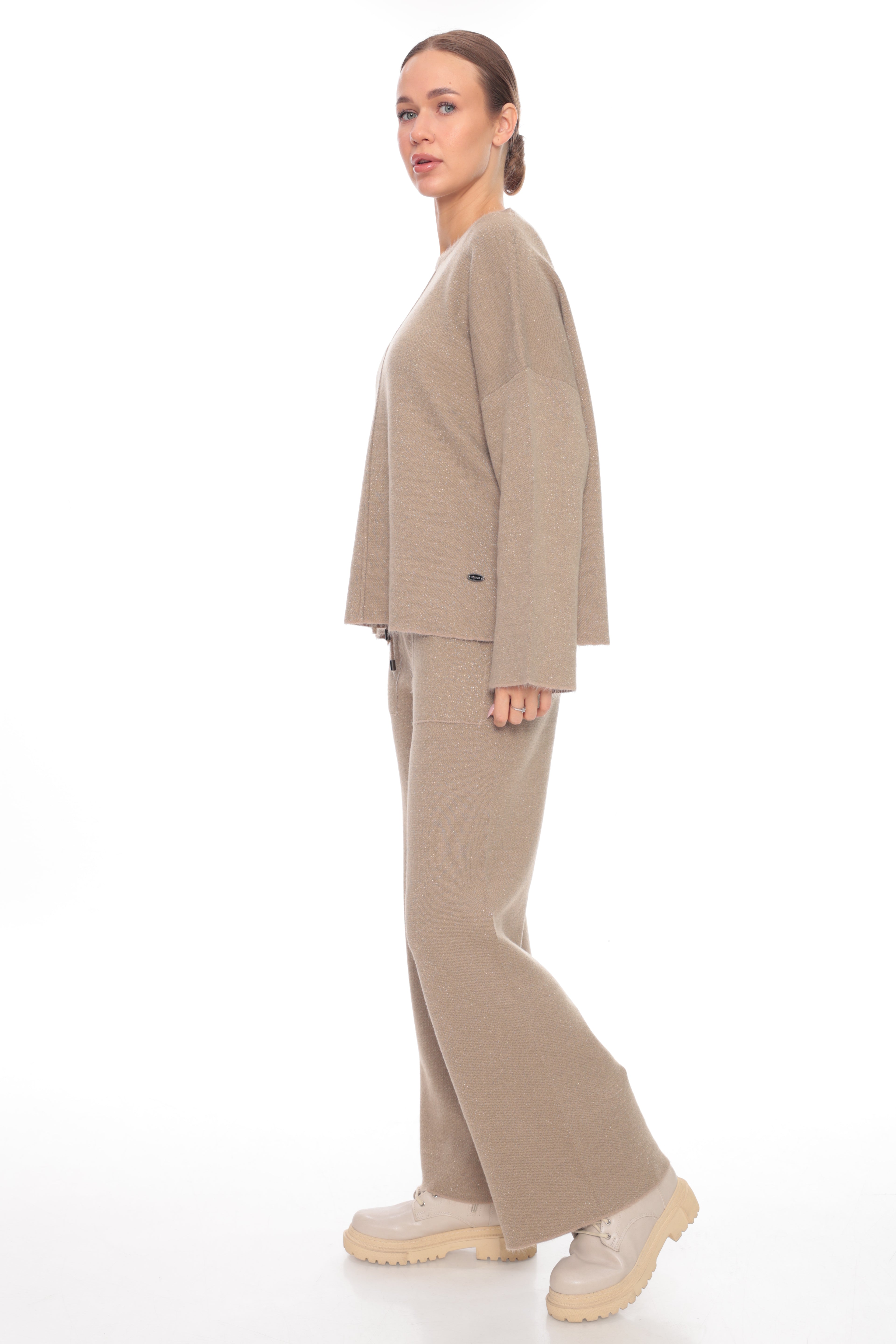 A woman modeling a matching beige knit lounge set consisting of a cropped long-sleeve top and wide-leg pants, paired with chunky off-white sneakers, against a solid white background.