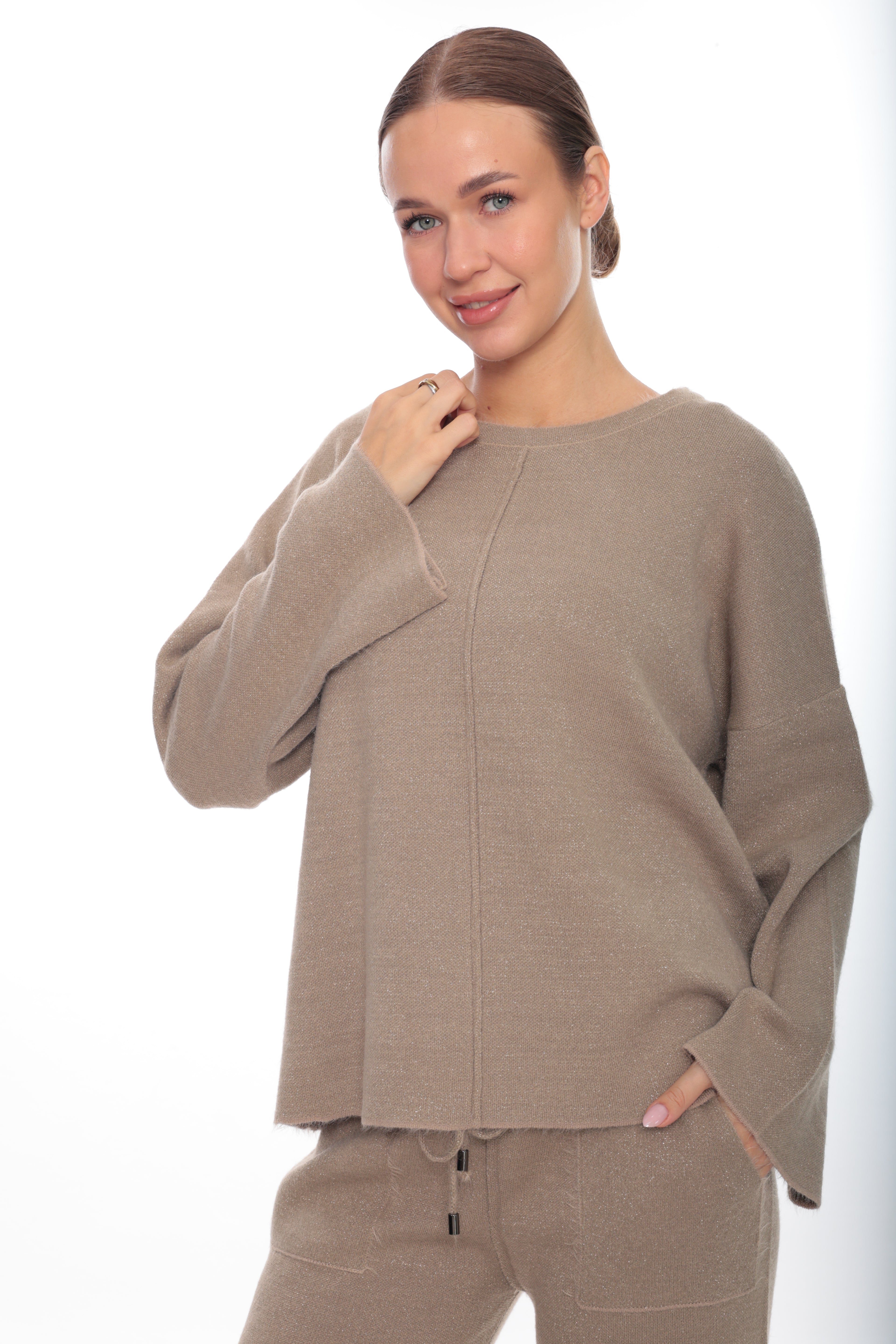 A woman modeling a taupe knit sweater and matching sweatpants against a plain white studio background.