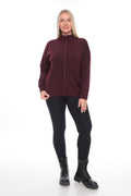 A woman modeling a maroon long-sleeve zip-up sweater, black leggings, and black boots against a plain white studio background.
