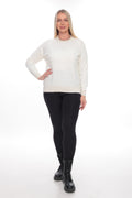 A woman modeling a cream-colored long-sleeve knit sweater, paired with black leggings and black combat boots, against a plain white studio background.