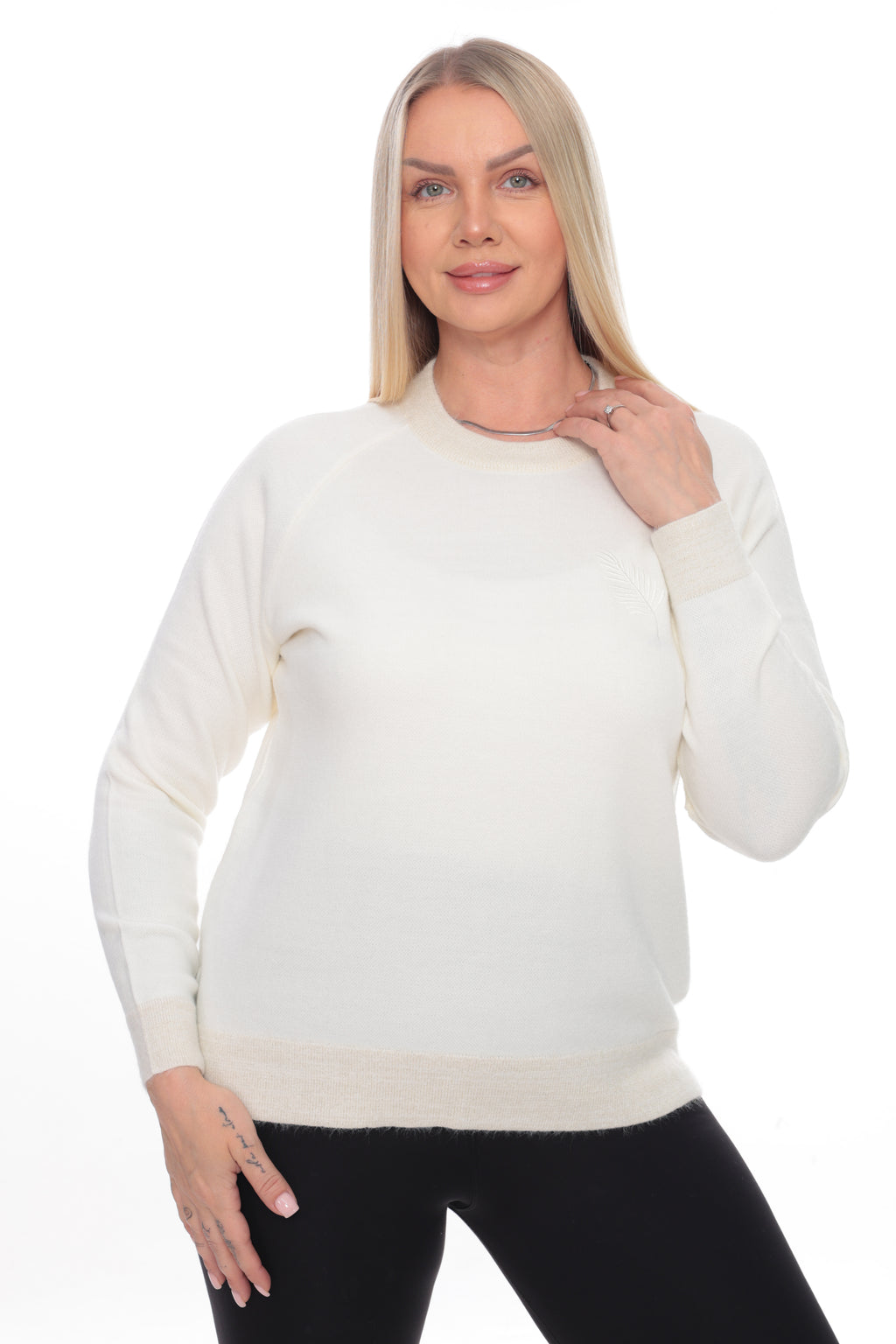 A blonde woman modeling a cream-colored long-sleeve crewneck sweater, paired with black pants, against a solid white background.