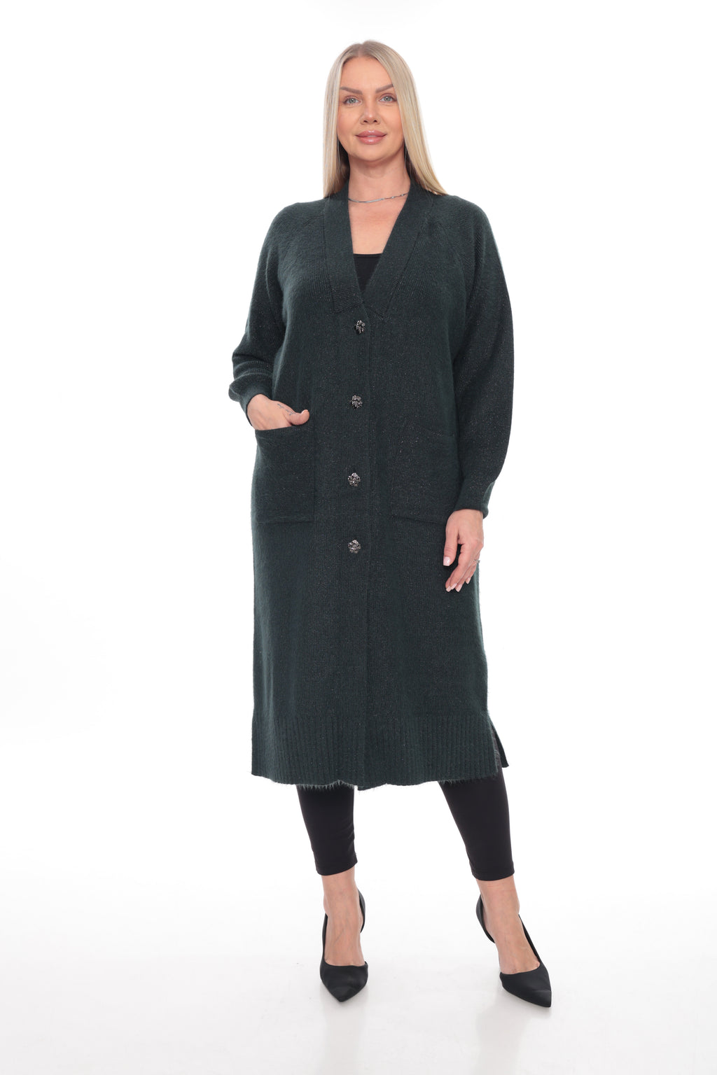 A woman modeling a long, dark green knit cardigan with front buttons and pockets, worn over a black top and black leggings, on a white studio background.