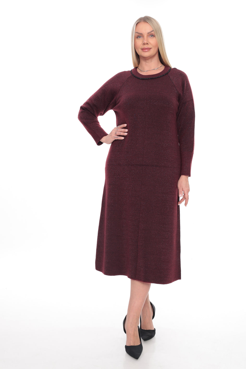 A woman modeling a long-sleeve knit midi dress in a deep burgundy color, paired with black pointed-toe heels, against a plain white studio background.