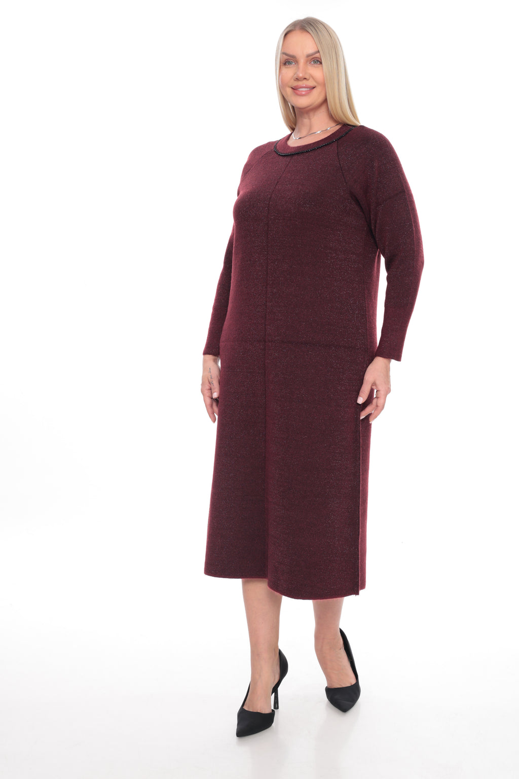 A woman modeling a long-sleeve knit midi dress in a deep burgundy color, paired with black pointed-toe heels, against a plain white studio background.
