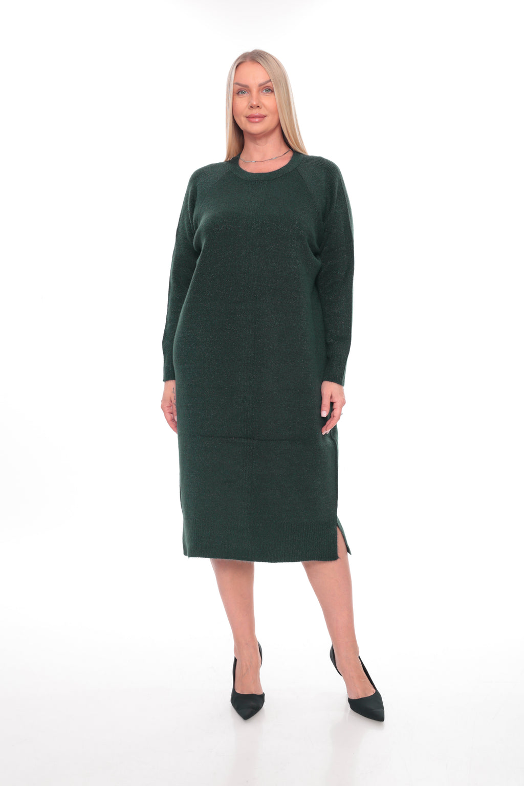 A woman modeling a dark forest green long-sleeve knit midi dress with a crew neck and side slits, paired with black pointed-toe heels, against a plain white studio background.