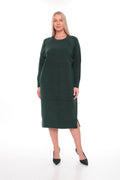 A woman modeling a dark forest green long-sleeve knit midi dress with a crew neck and side slits, paired with black pointed-toe heels, against a plain white studio background.