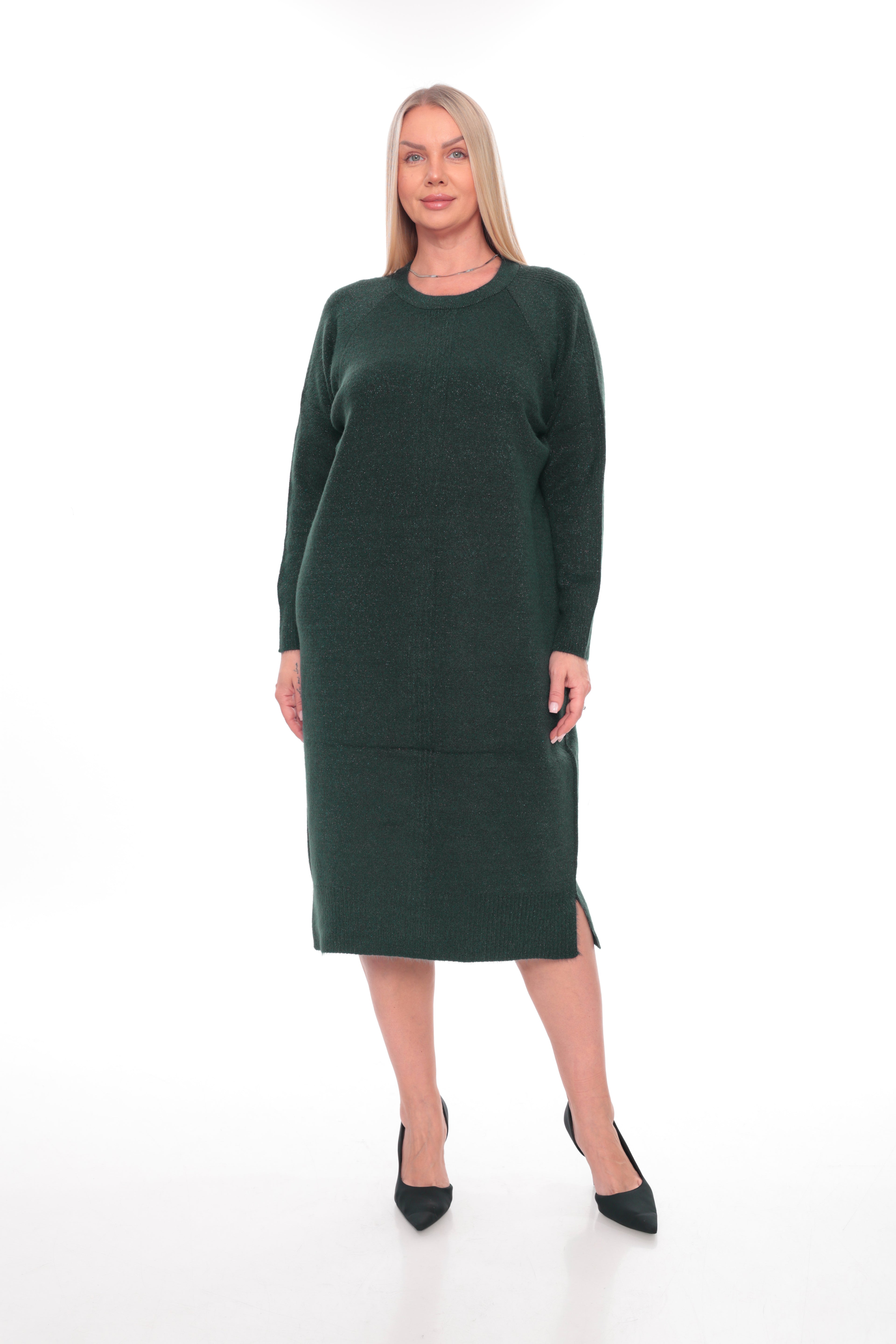 A woman modeling a dark forest green long-sleeve knit midi dress with a crew neck and side slits, paired with black pointed-toe heels, against a plain white studio background.