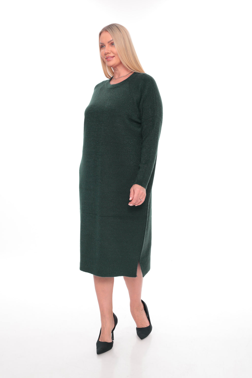 A woman modeling a dark forest green long-sleeve knit midi dress with a crew neck and side slit, paired with black pointed-toe heels, against a plain white studio background.