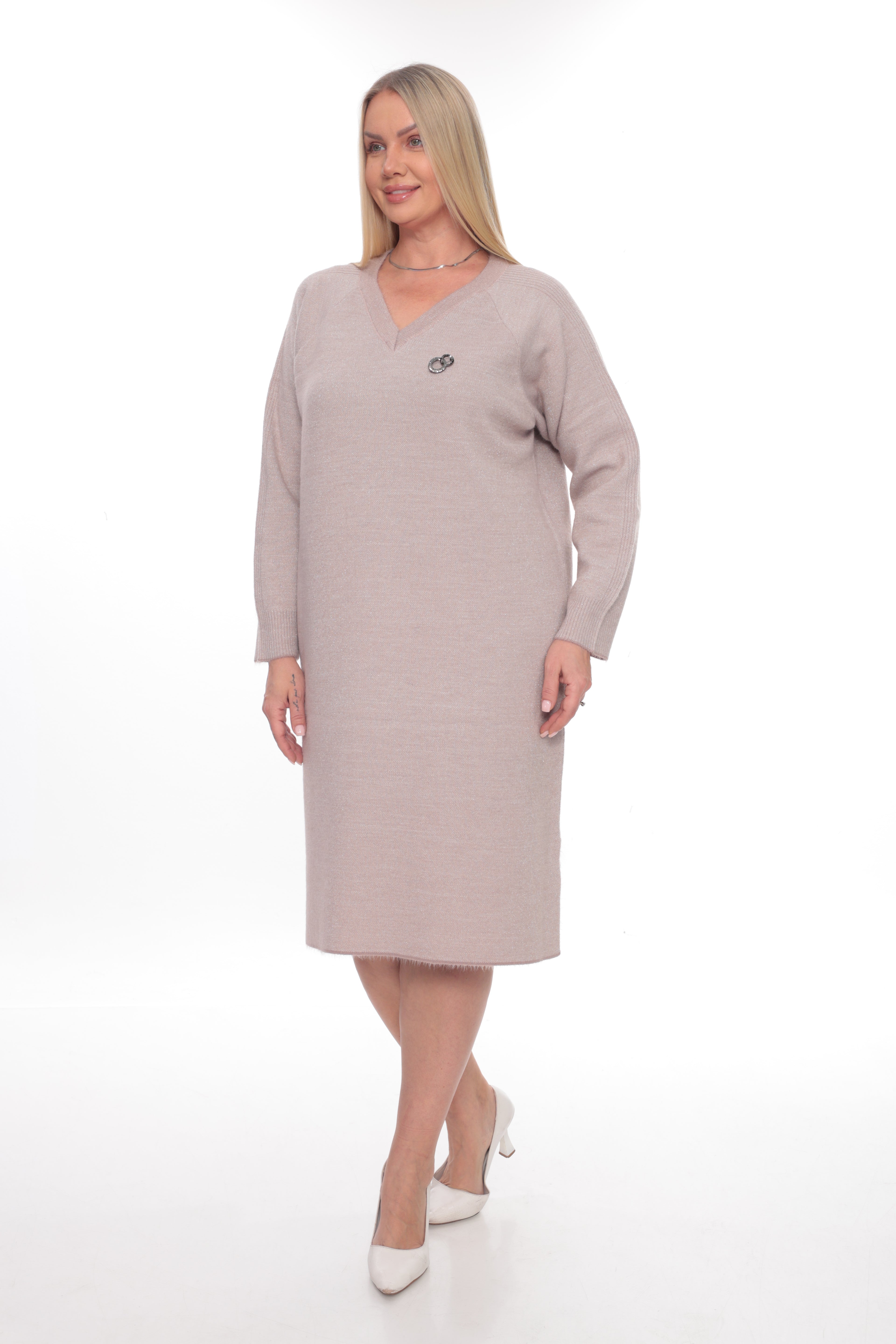 A woman modeling a long-sleeve V-neck knit dress in a light taupe-beige color, paired with white heels, against a plain white studio background.