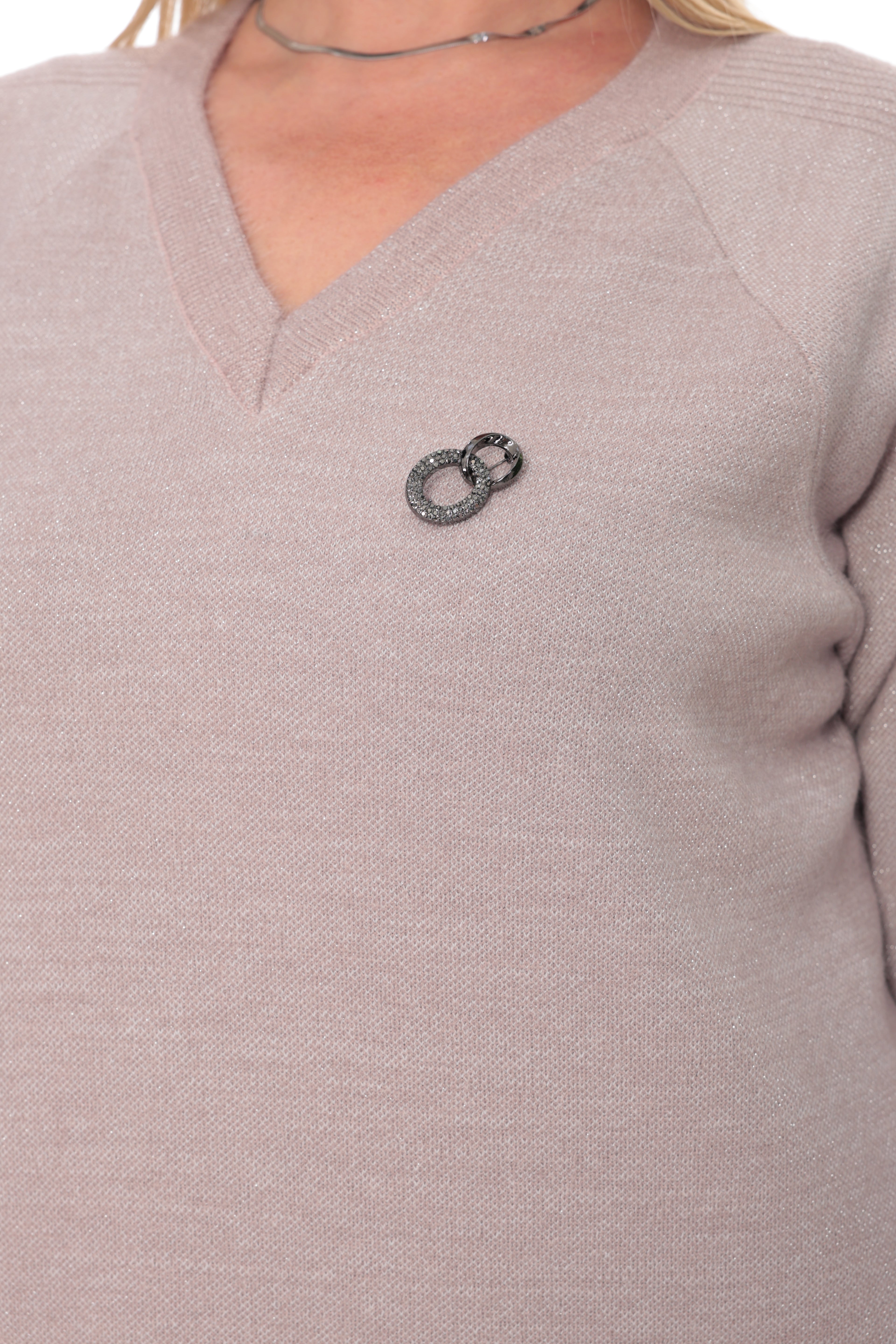 A close-up of a person wearing a light blush pink V-neck knit sweater with a small silver-toned ring brooch on the chest.