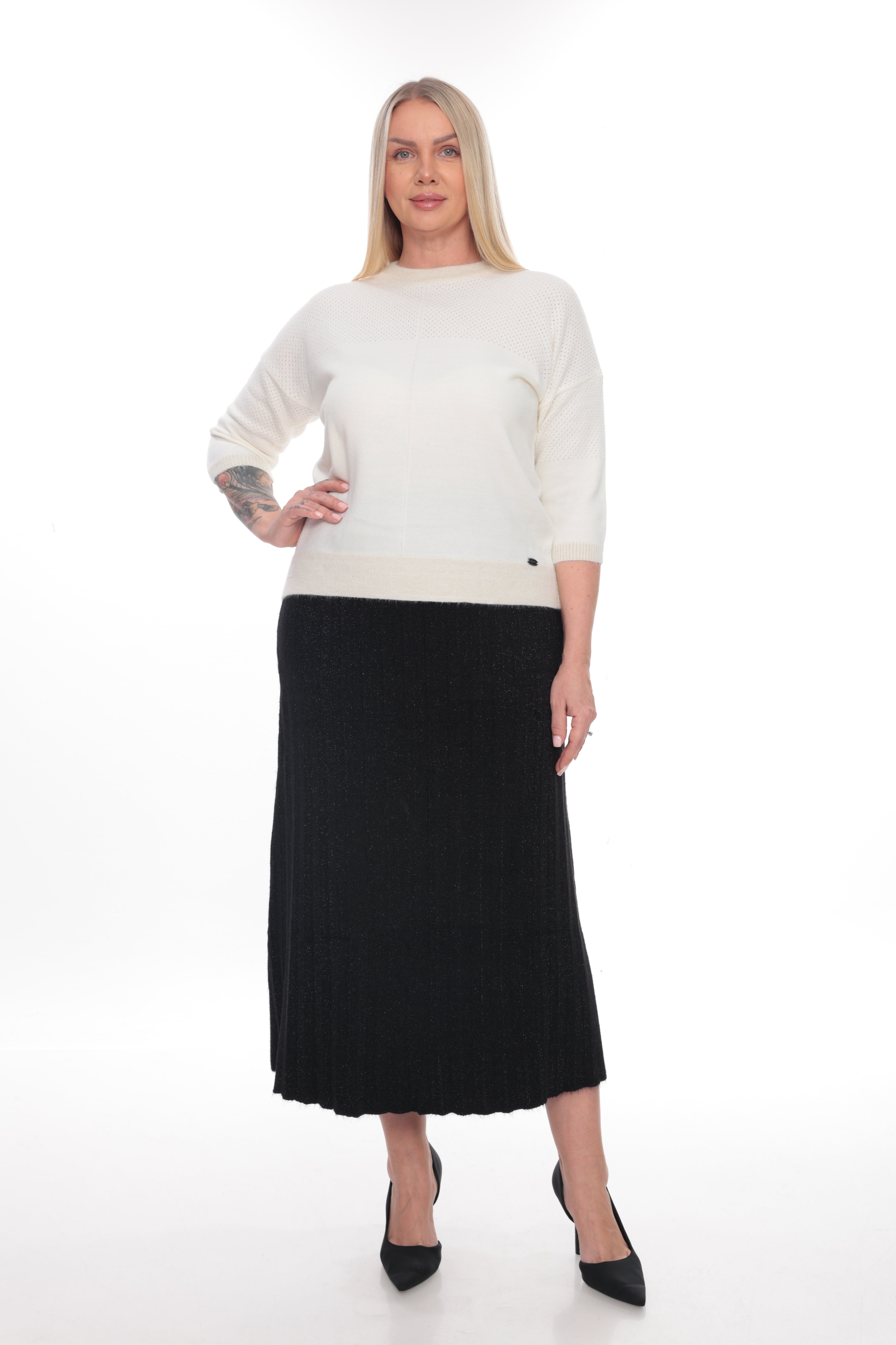 A woman modeling a cream knit sweater and a black midi skirt against a plain white studio background.