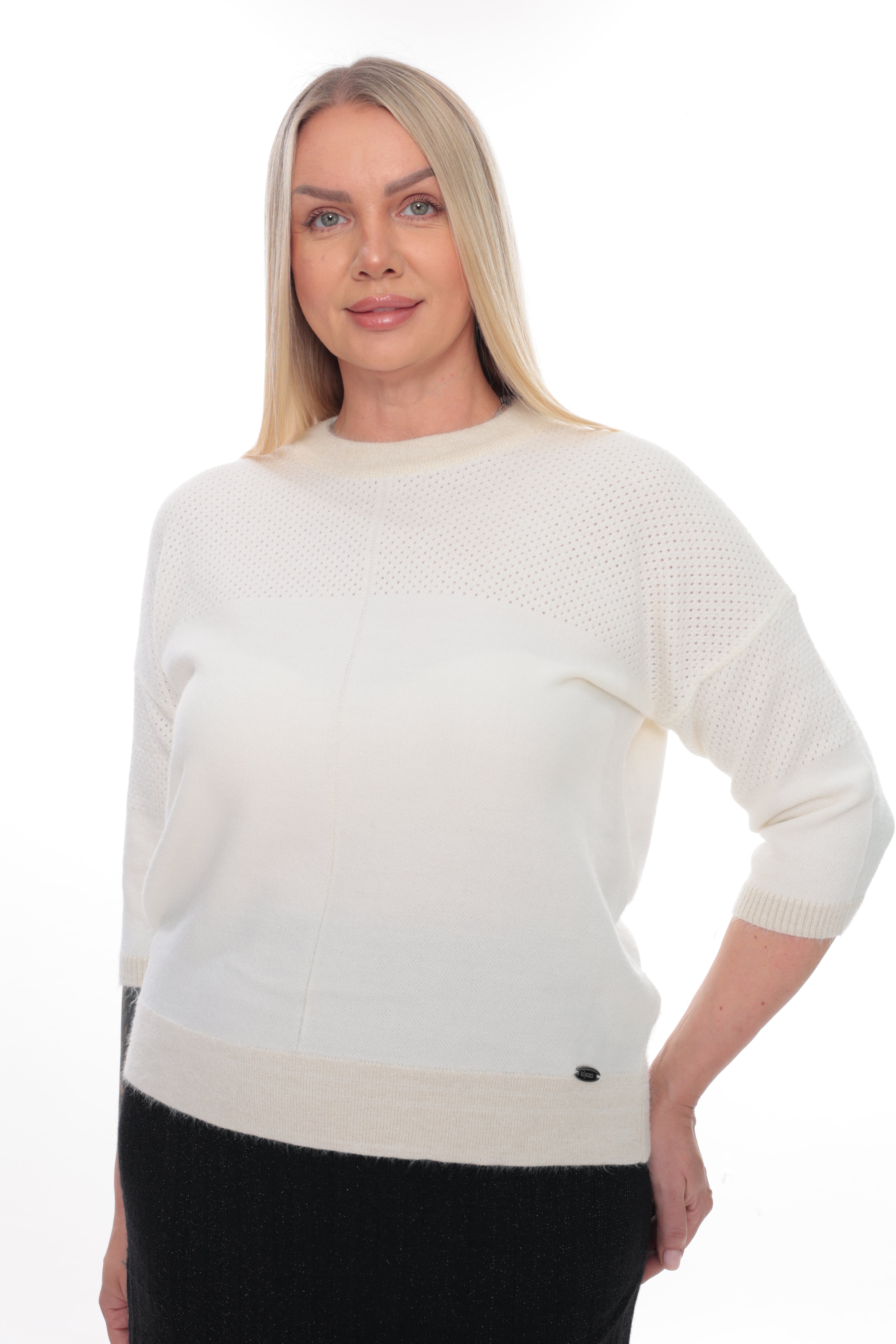 A blonde woman wearing a cream-colored knit sweater with a textured openwork pattern on the upper chest and sleeves, paired with a black skirt, against a plain white background.