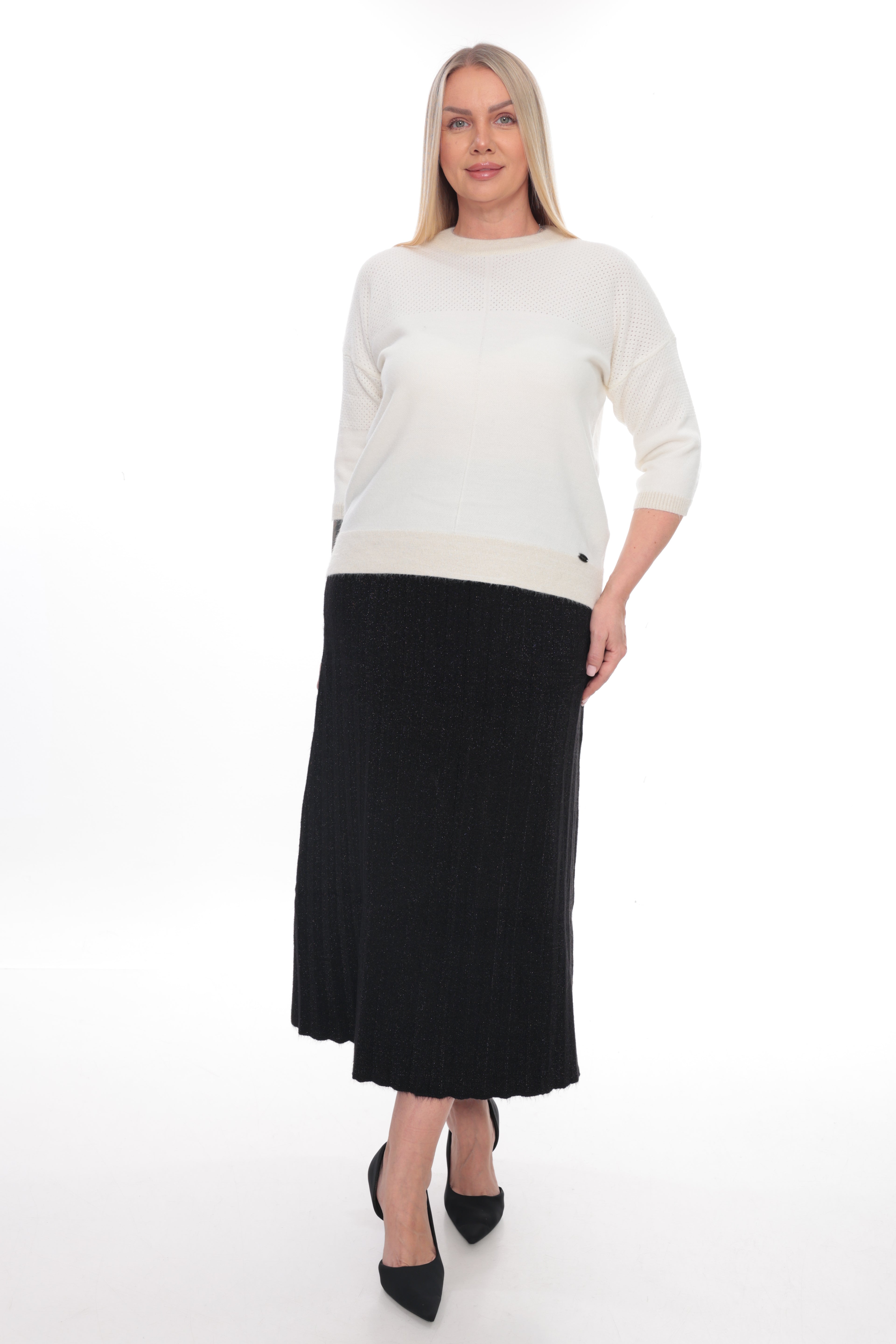 A woman modeling a cream knit sweater with three-quarter sleeves and a black pleated midi skirt, paired with black pointed-toe heels, against a plain white studio background.