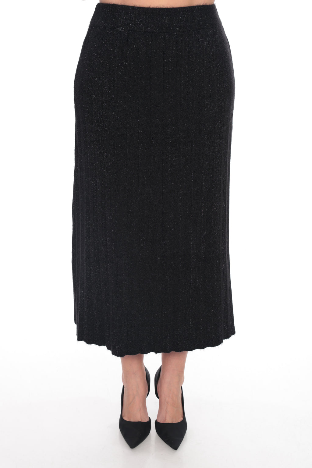 A black ribbed knit midi skirt shown on a model from the waist down, paired with black pointed-toe heels, against a plain white studio background.
